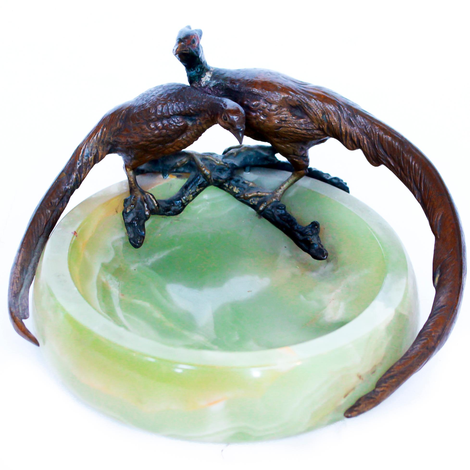 An early 20th century vide poche with two bronze pheasants, a male 'cock' and a female 'hen', perched upon bronze branches with their long tails encircling a green onyx dish.

Dimensions: H 8cm D 18cm

Origin: English

Date: circa 1920

Item