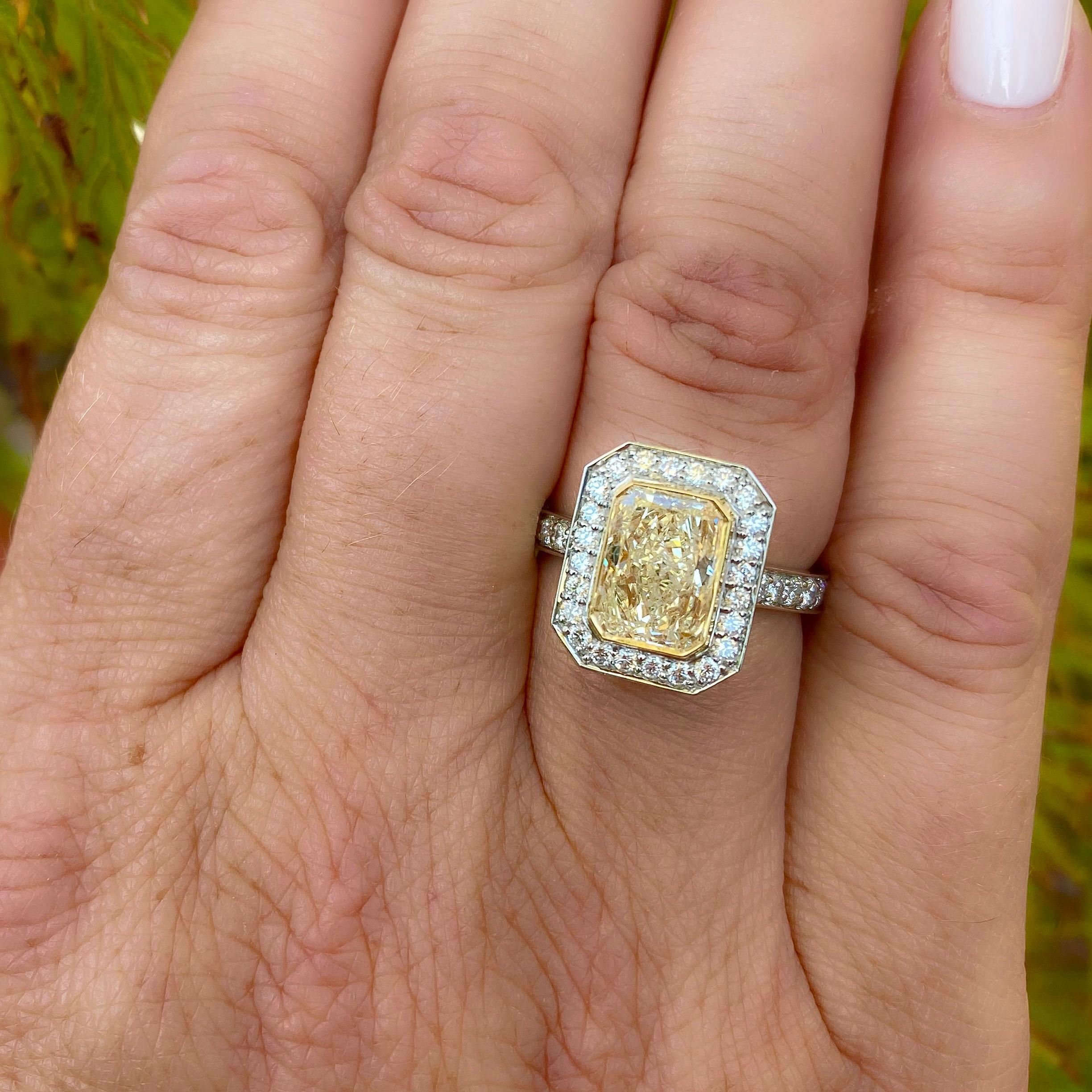 Elegant and classic, this platinum ring centers a 2.21 carat radiant-cut natural yellow diamond bezel-set in 18k yellow gold for added beauty, surrounded by 42 near colorless round brilliant-cut diamonds, for a total weight of 2.81 carats. The ring