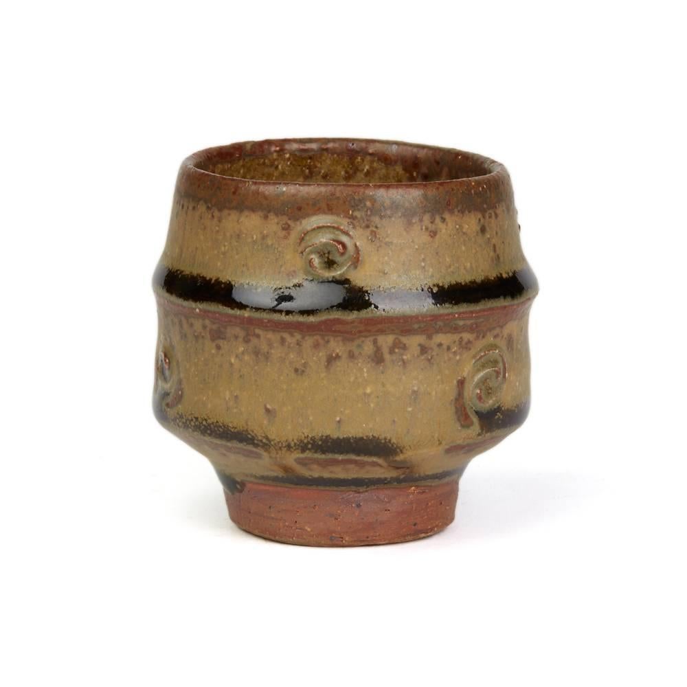 A fine vintage British studio pottery yunomi (teacup) by renowned potter Phil Rogers (b. 1951) and made in Powys, Wales. The stoneware yunomi is of rounded cylindrical shape with a horizontal band the body impressed with spiral details standing on a