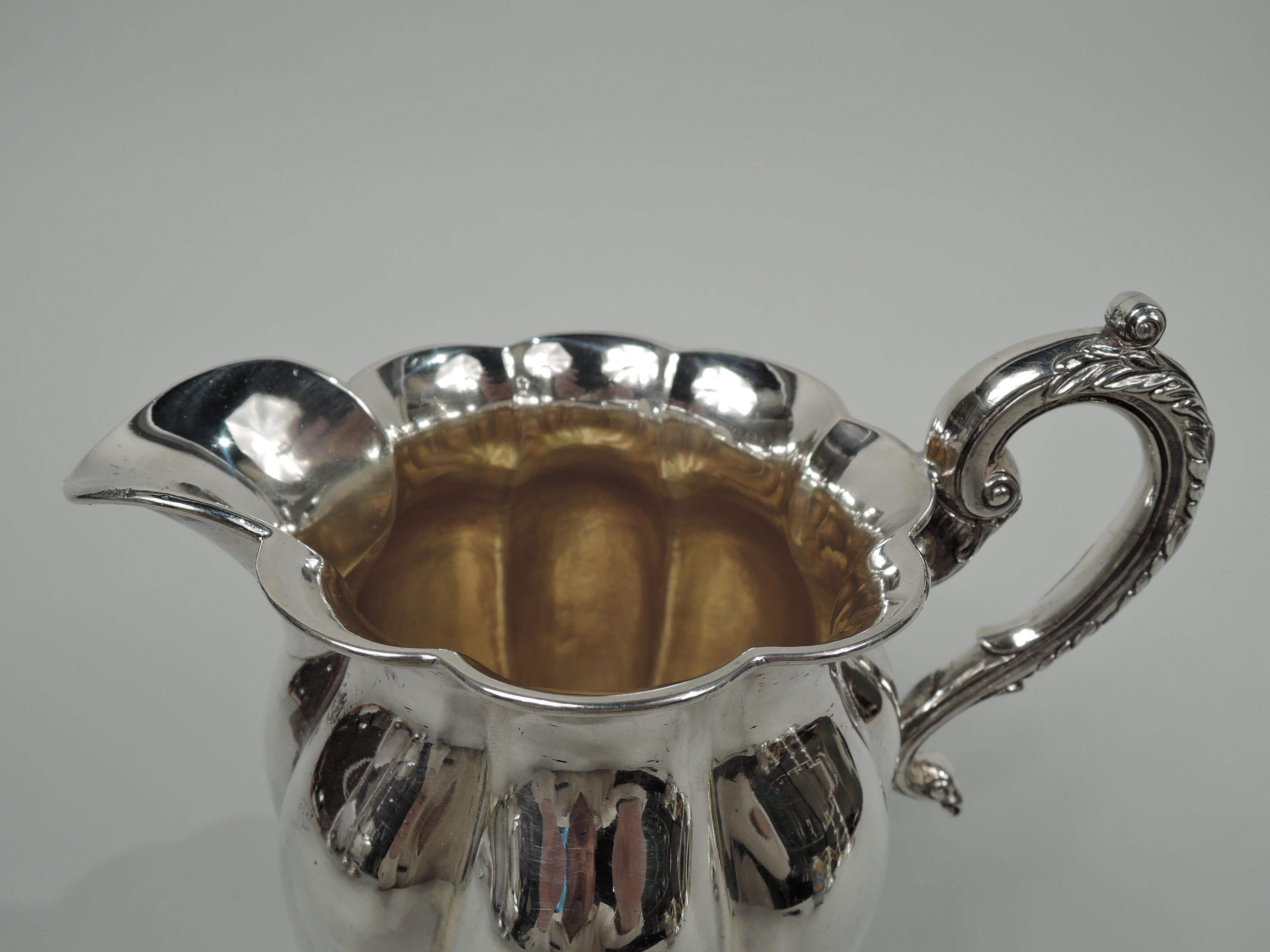 Classical coin silver creamer. Made by Thomas Fletcher in Philadelphia, ca 1830. Lobed ovoid body with scalloped rim and u-spout. Leaf-capped high-looping s-scroll handle. Raised foot; serpentine rim with leaf, shell, and flower ornament on stippled