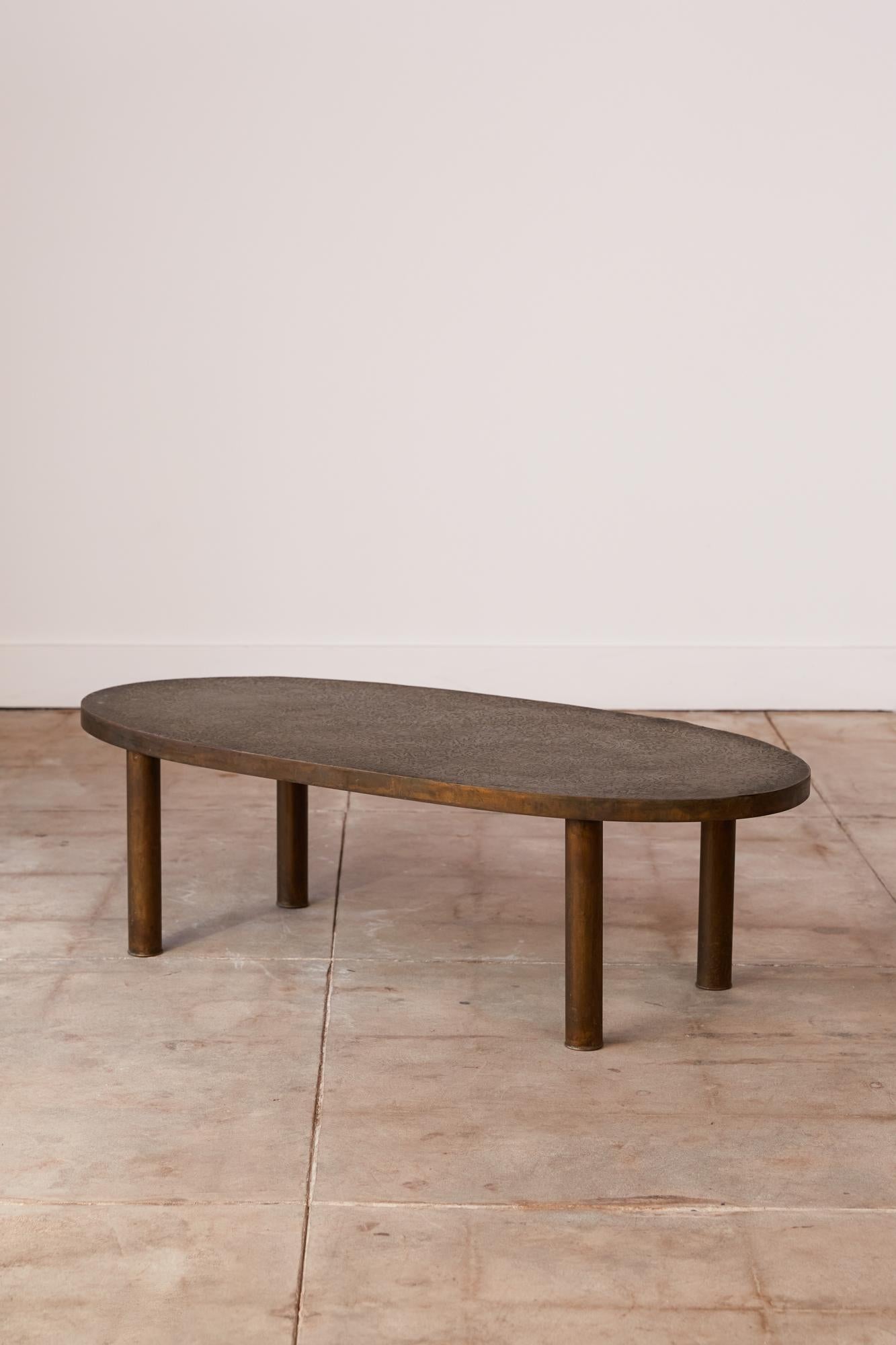 A highly collectible acid etched bronze coffee table by Philip and Kelvin Laverne. The oval shaped table features their 