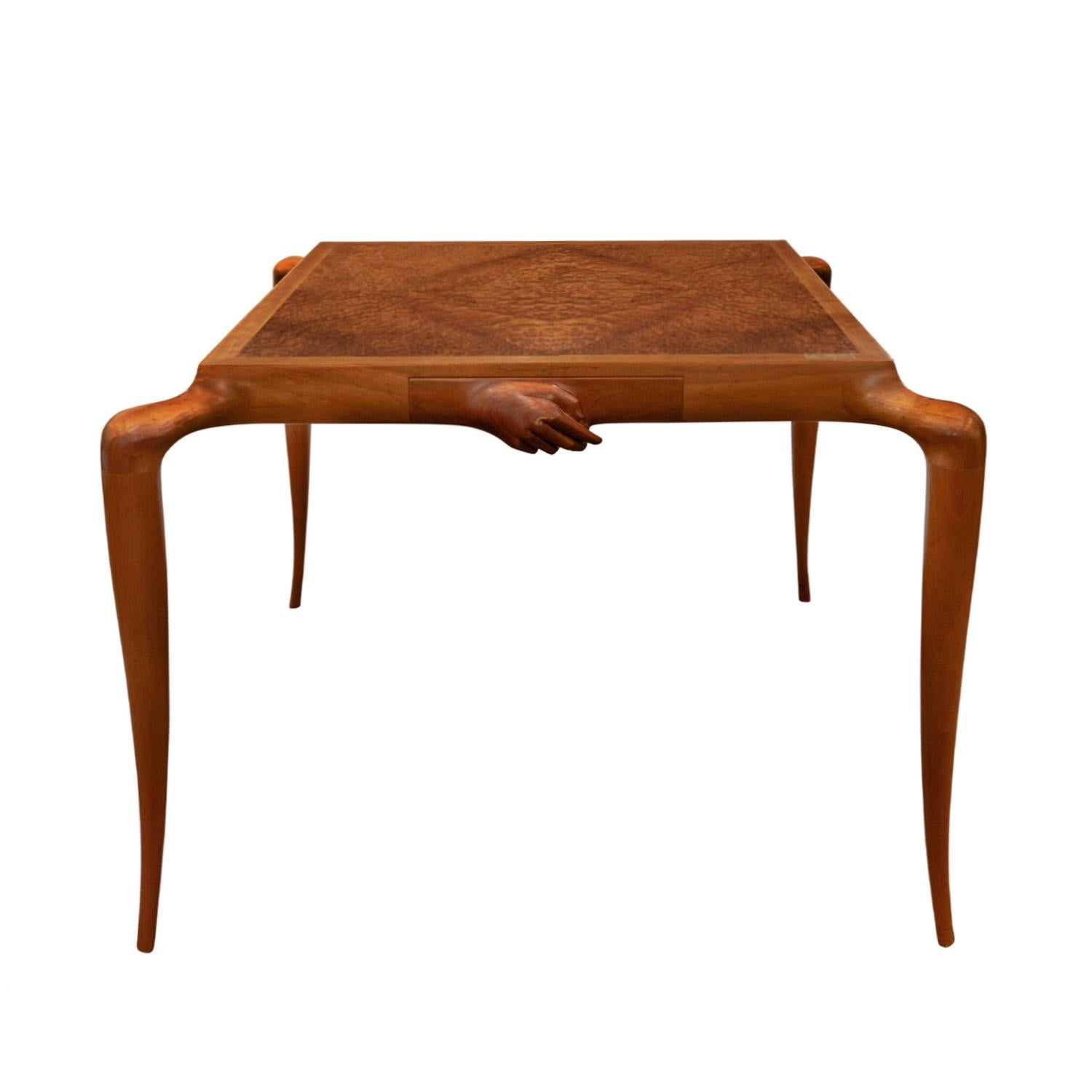 One-of-a-kind sculpture game table in teak with book-matched Carpathian elm top with 2 drawers on opposite sides, each with a carved articulated hand over it, by Philip LaVerne, American 1966 (signed on top “Philip LaVerne”). The sculpted tapering