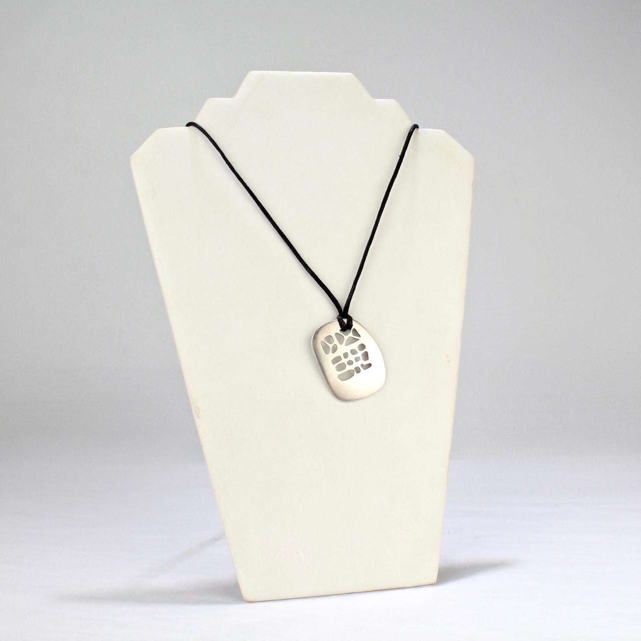 A simple modernist pendant by Philip Morton in sterling silver.

Of slightly convex tablet form with organic pierced openings suspended by a later associated black cord.

Philip Morton was a founding member of SNAG, the Society of North American