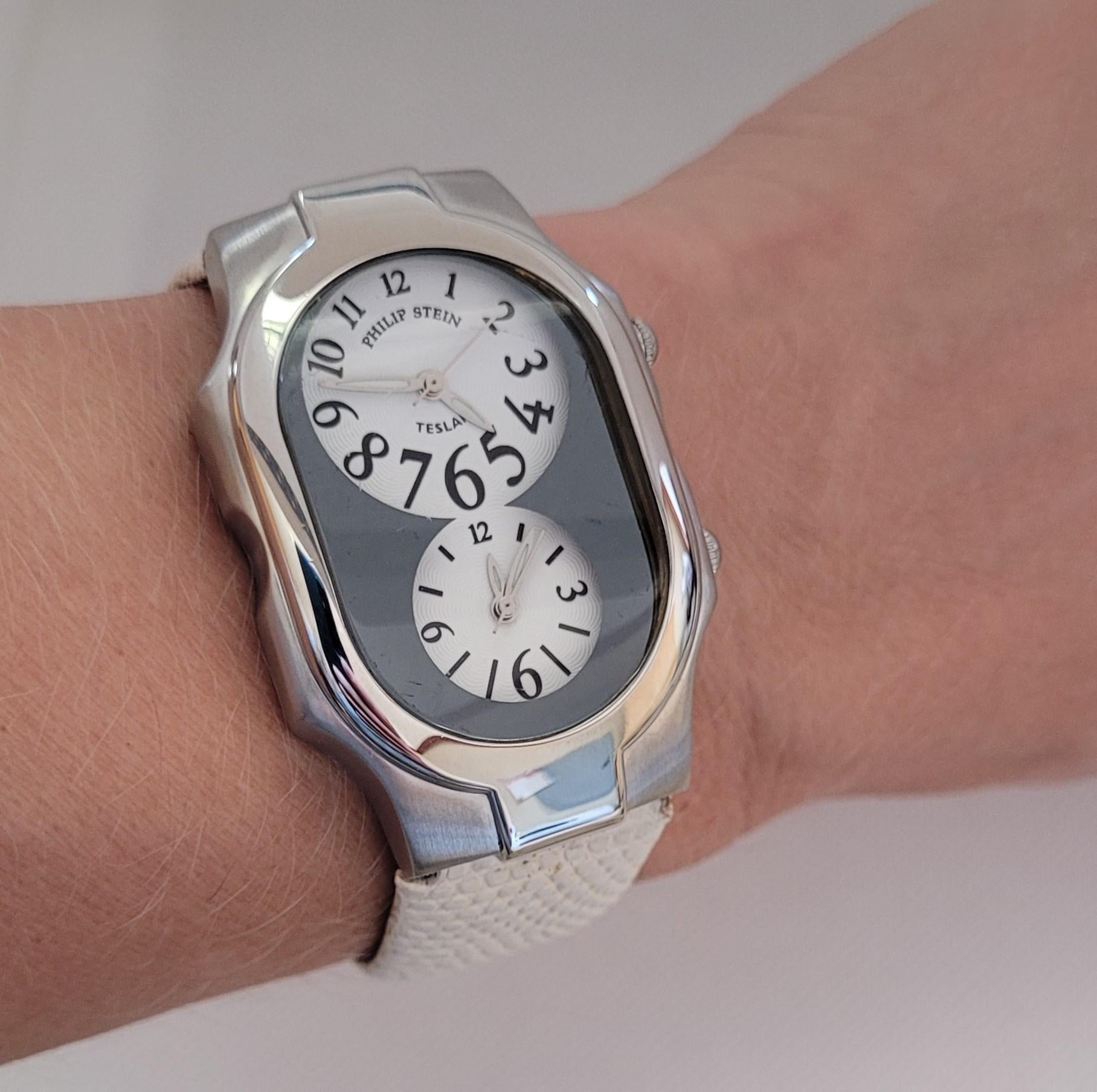 Philp Stein Teslar watch with a dual watch face and white leather strap. The case has a polished and satin finish and is 48mm x 30mm x 10mm in size with a two-tone gray and white face. The crystal has light scratches that are not obvious. The case