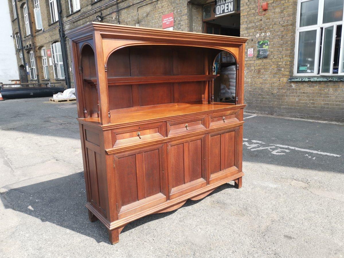 Philip Webb per Morris & Co. Rara credenza Arts & Crafts in noce, con piano ad arco e supporti a pilastro, ripiano superiore centrale arretrato con scanalature portapiatti, un cassetto singolo e uno doppio con maniglie in ottone e tre armadietti