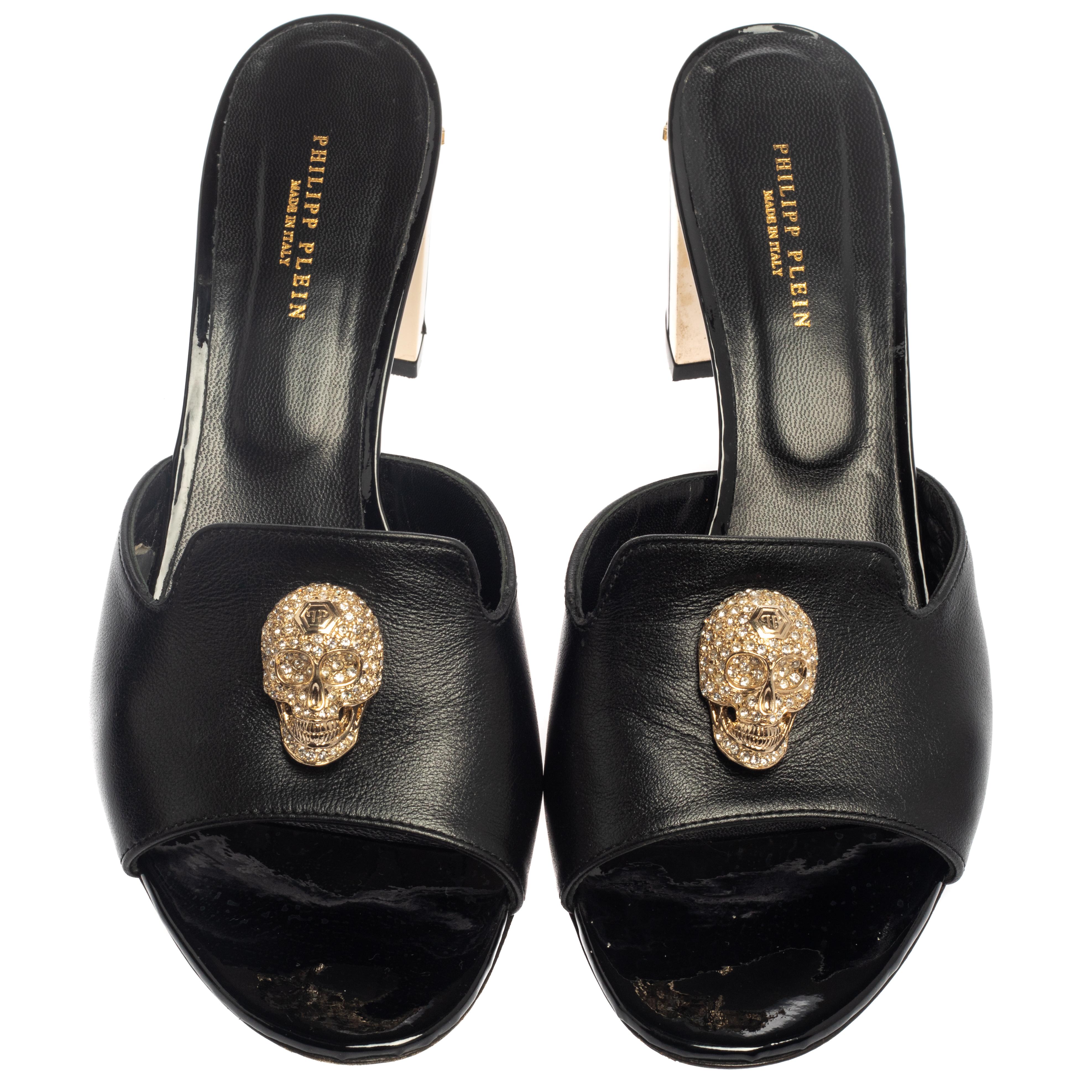 How pretty are these slide sandals from Philipp Plein! The black sandals are crafted from leather and feature an open toe silhouette. They flaunt single vamp straps with skull embellishments and 7 cm block heels with the logo adorning them.