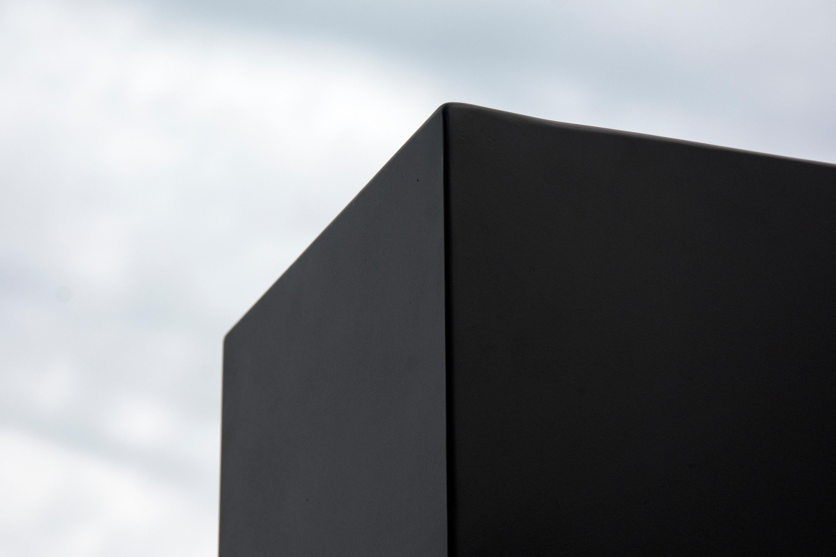 Une sculpture extérieure rectangulaire en acier de couleur noire est divisée en trois parties, comme un puzzle, les bords étant polis et réfléchissants. Ce montant de sept pieds est reflété par trois formes de flaques d'acier réfléchissantes