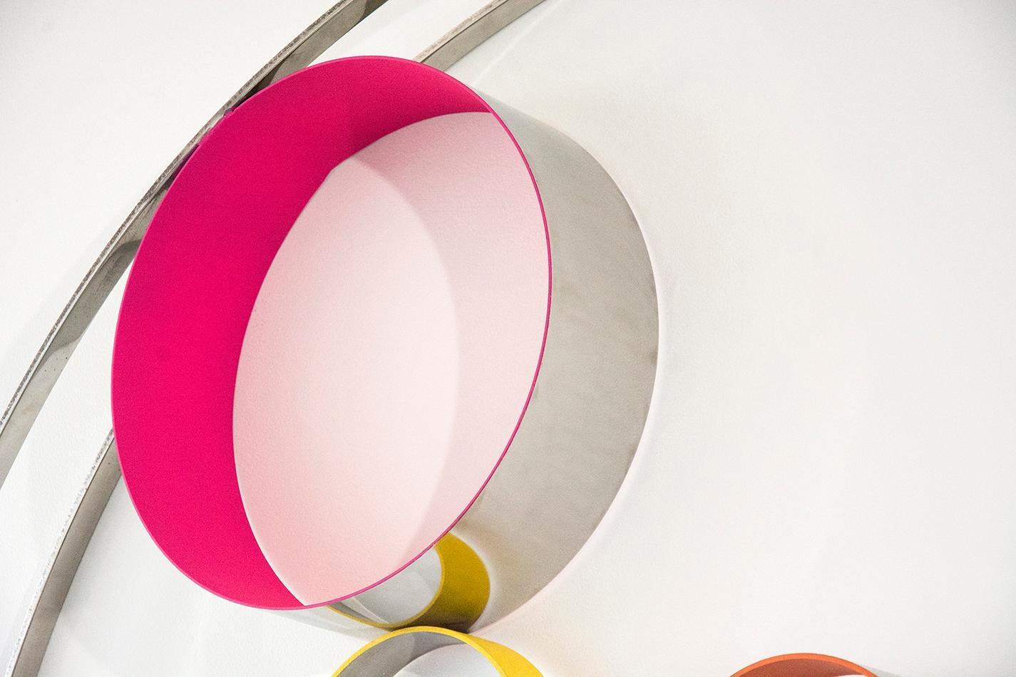 A playful collection of steel rings and disks bubble and swirl within the confines of two steel hoops. The elements of this modernist inspired wall tondo by Philippe Pallafray are polished to a high sheen and patinated in hot pink, lemon and orange.