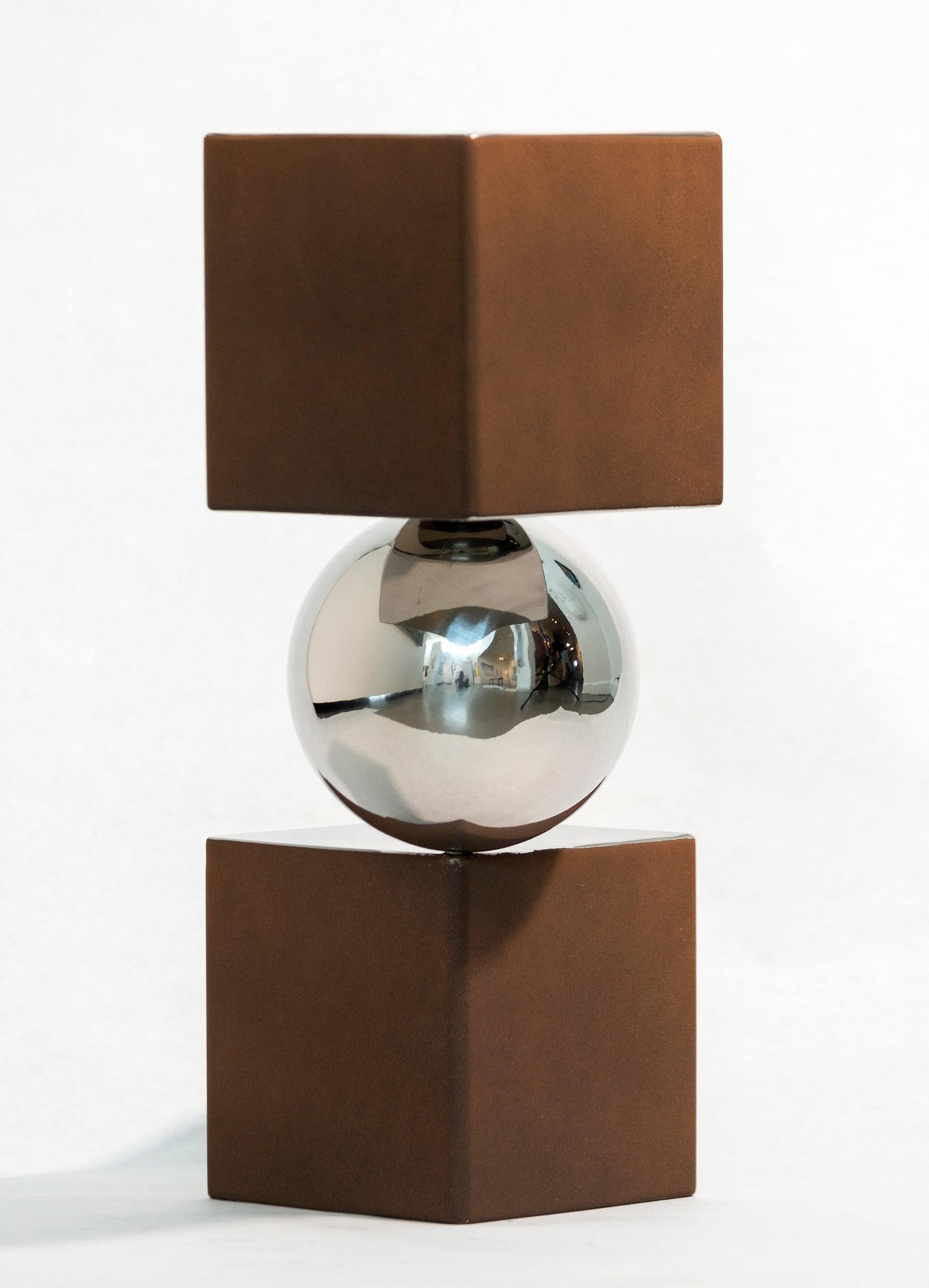 Une sphère en aluminium poli se tient astucieusement en équilibre entre deux cubes de couleur rouille et argent dans cette sculpture de table moderne et dynamique de Philippe Pallafray. Equilibre