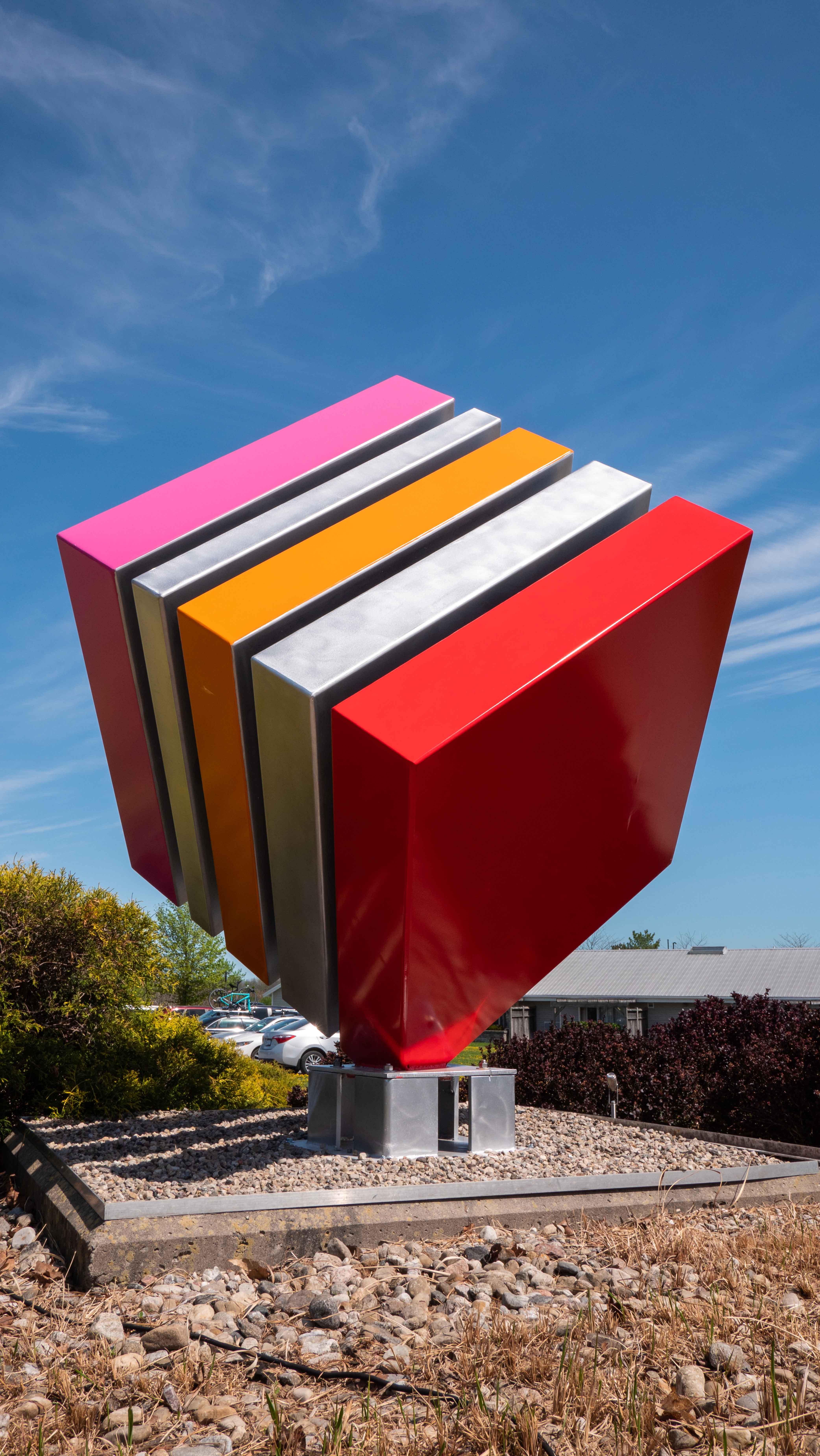 Philippe Pallafray’s latest sculpture—an eye-popping candy-coloured large steel cube—each stripe painted in bright red, orange and pink balances on one corner. The Quebec artist designs pop art pieces that reflect the duality of nature and the