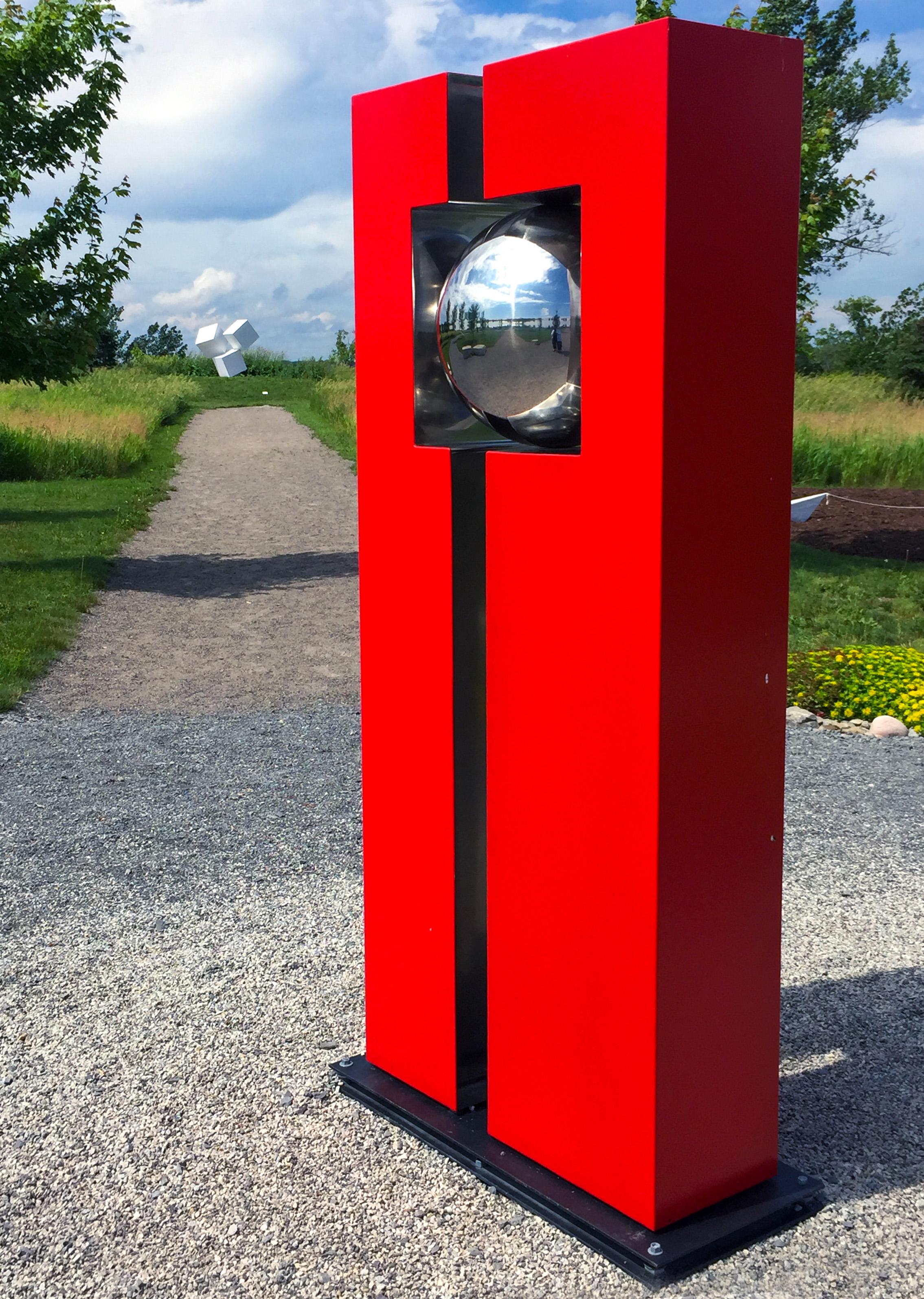 Una palla in acciaio inossidabile lucido è incorniciata dal rosso cardinale in questa scultura geometrica per esterni dell'artista francese Philippe Pallafray. La scultura industriale e minimalista è in netto contrasto con l'ambiente naturale, ma lo