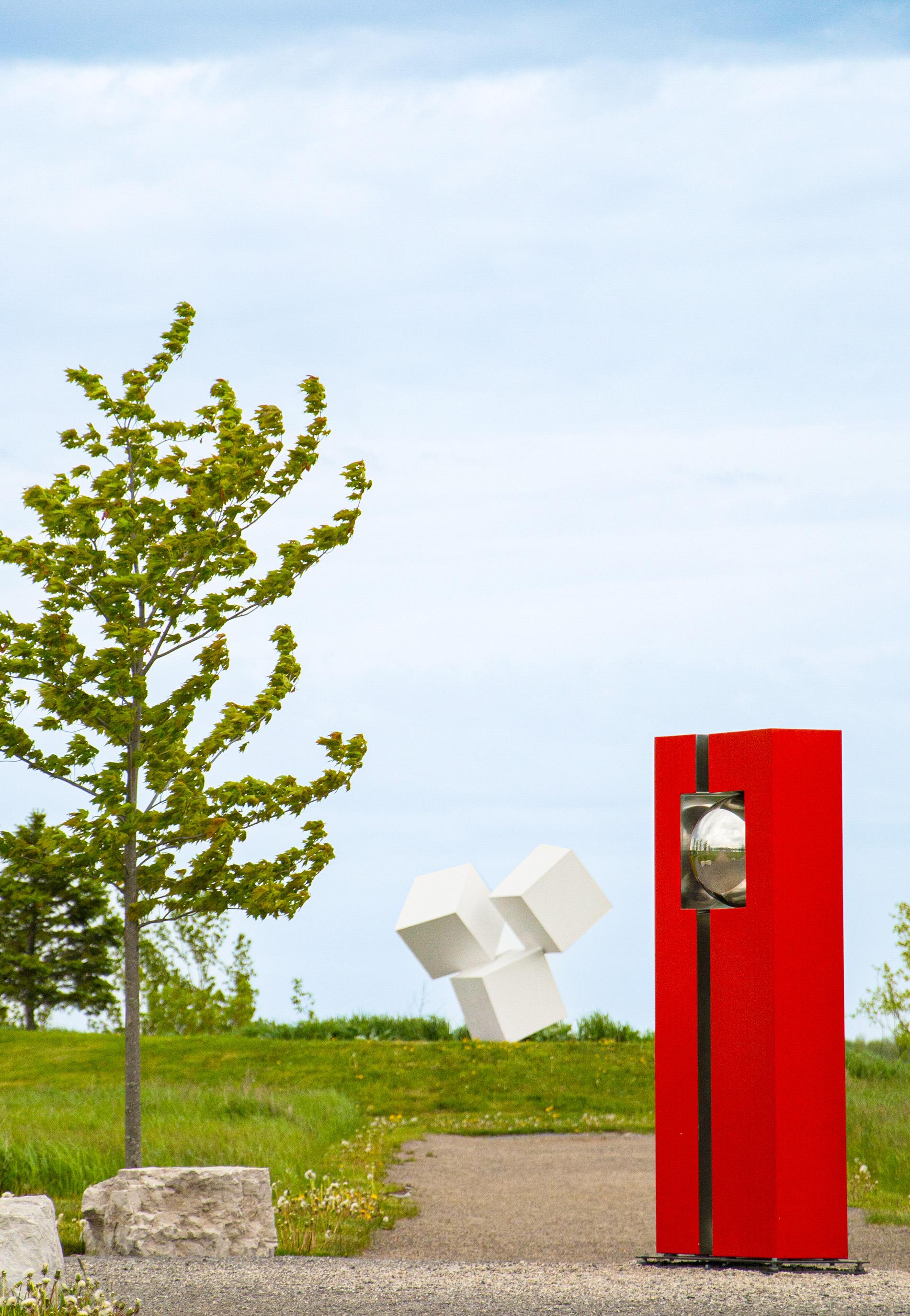 A polished stainless steel ball is framed by cardinal red in this outdoor geometric sculpture by French artist Philippe Pallafray. The industrial, minimalist sculpture sits in dramatic contrast to the natural environment and yet also mirrors it back