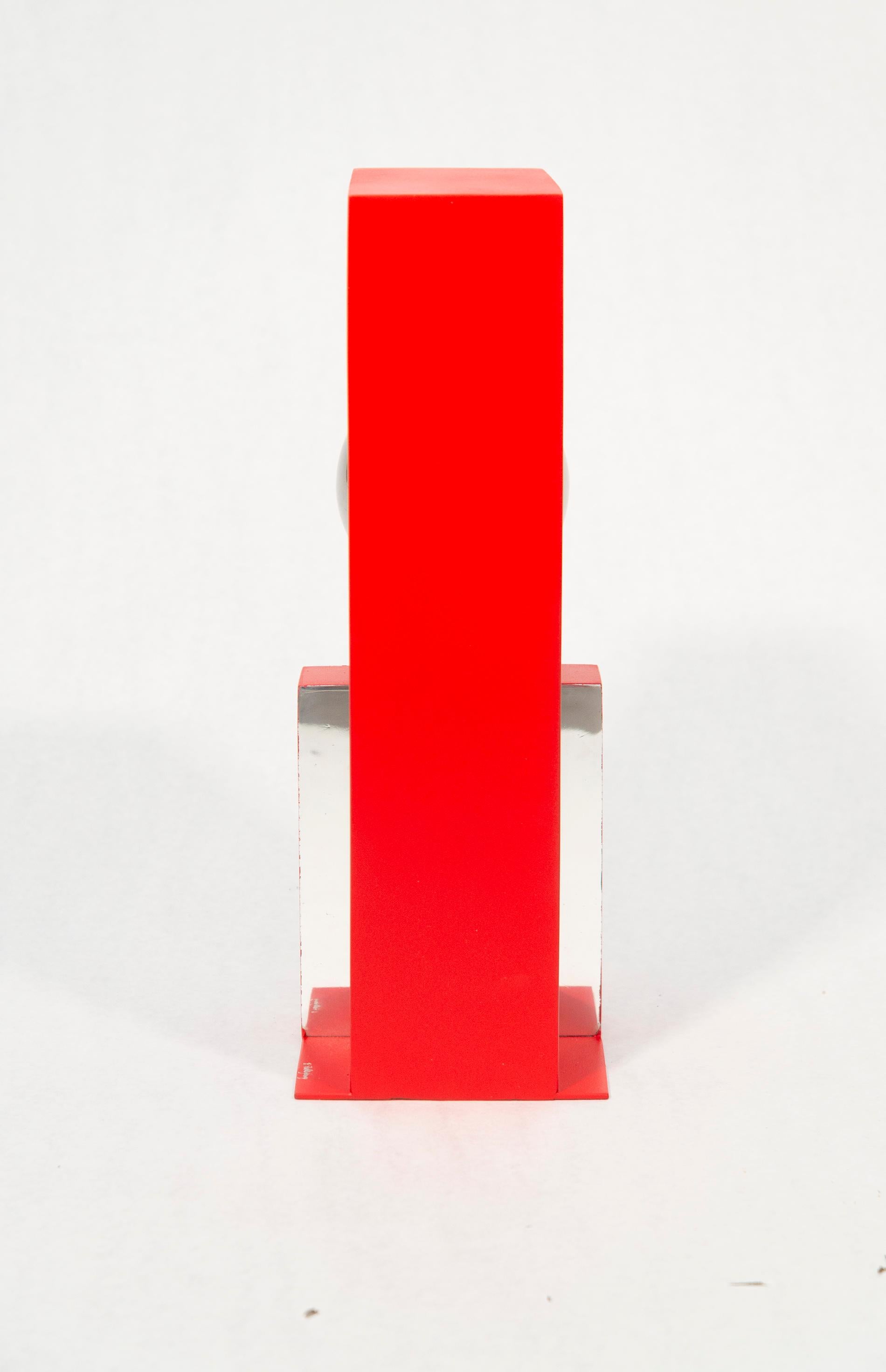 A highly polished stainless-steel ball framed by a rectangular cardinal red form appears to float in this dynamic table-top sculpture by Philippe Pallafray. The industrial, modern minimalist sculpture sits in dramatic contrast to the natural