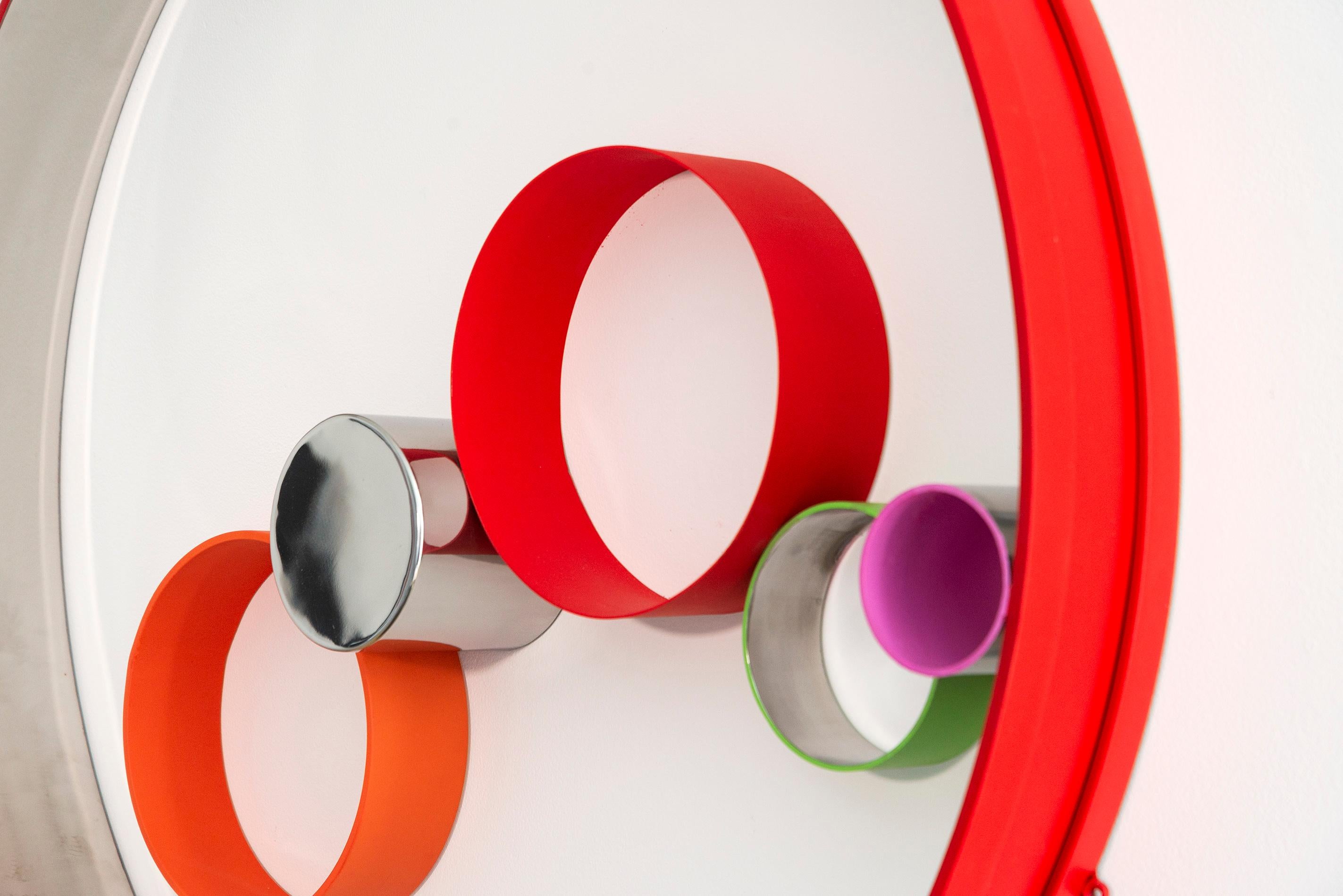 Painted in vivid colours, this intriguing modern metal wall sculpture was hand forged by Philippe Pallafray. Six stainless steel rings of varying sizes—painted in red, orange, yellow, green and pink appear to float inside a large red ring. The