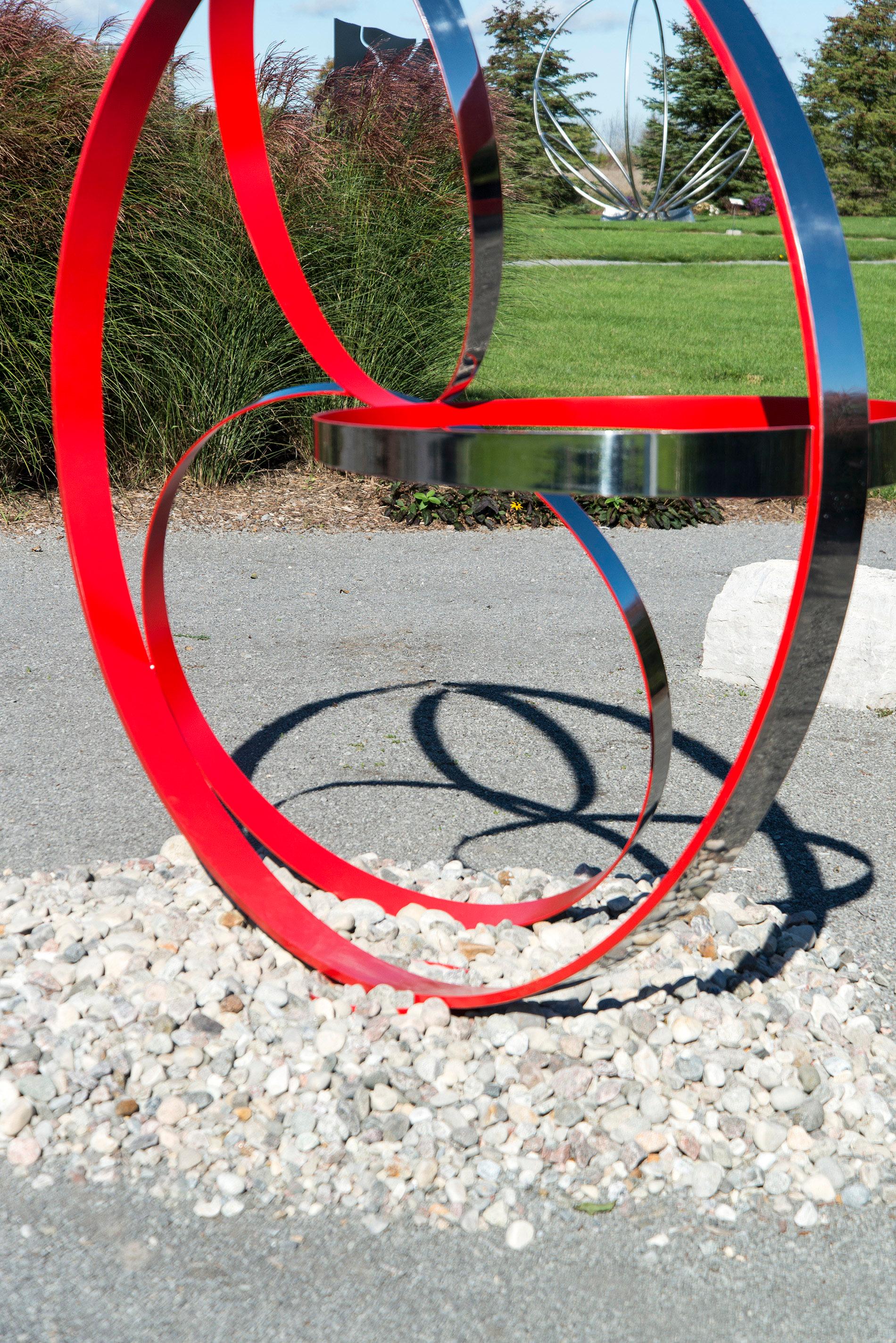Vier Ringe aus Edelstahl, eine Seite in Mohnrot, werden von Philippe Pallafray zu einer eleganten Komposition für den Außenbereich zusammengestellt. Diese minimalistische Skulptur spielt mit dem Raum, umrahmt die Landschaft und steht doch im