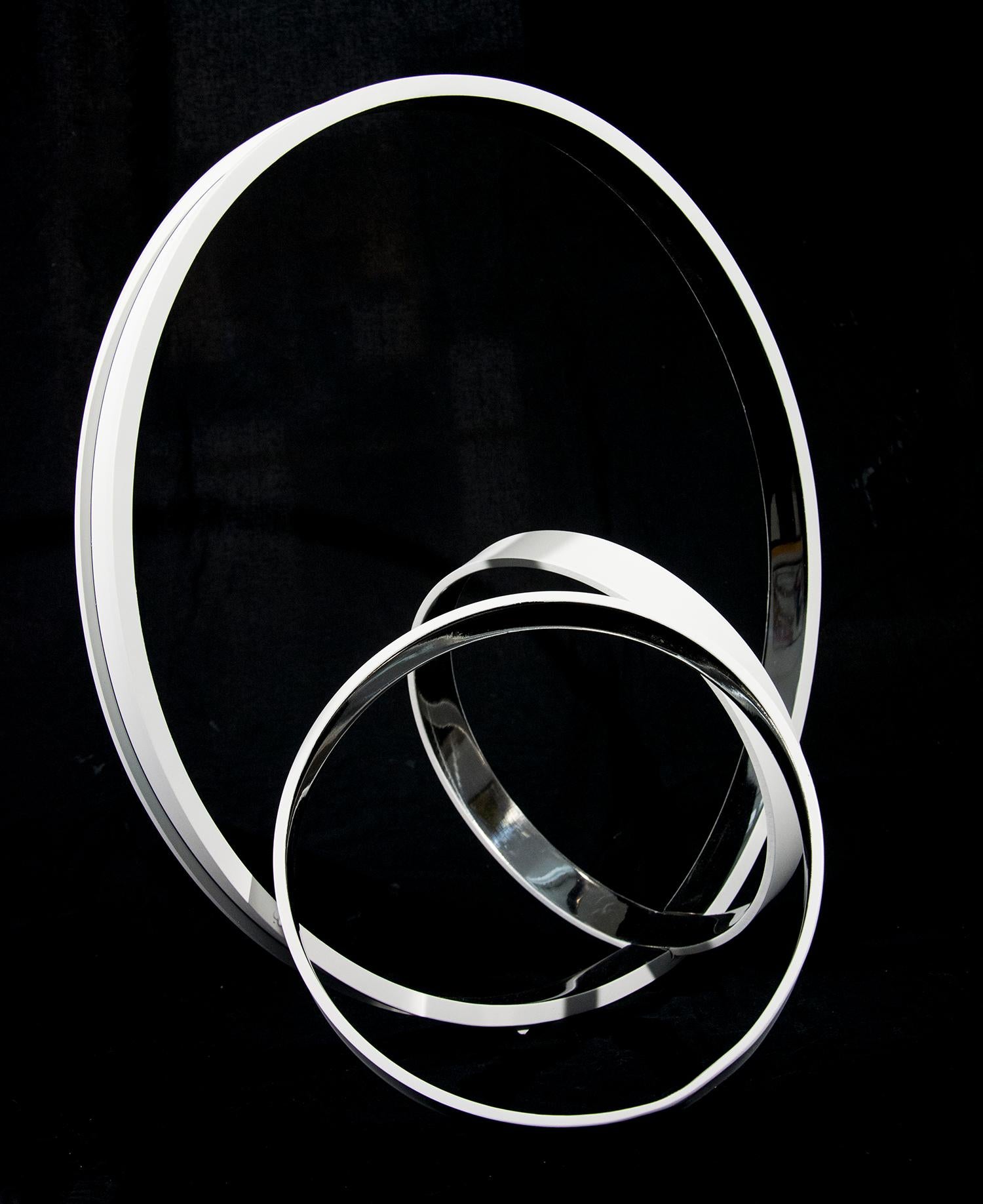 Des anneaux d'acier inoxydable, polis d'une grande brillance à l'extérieur et d'un blanc mat à l'intérieur, se croisent à des angles dynamiques dans cette élégante sculpture de Philippe Pallafray. Son travail est conçu pour représenter la dualité de