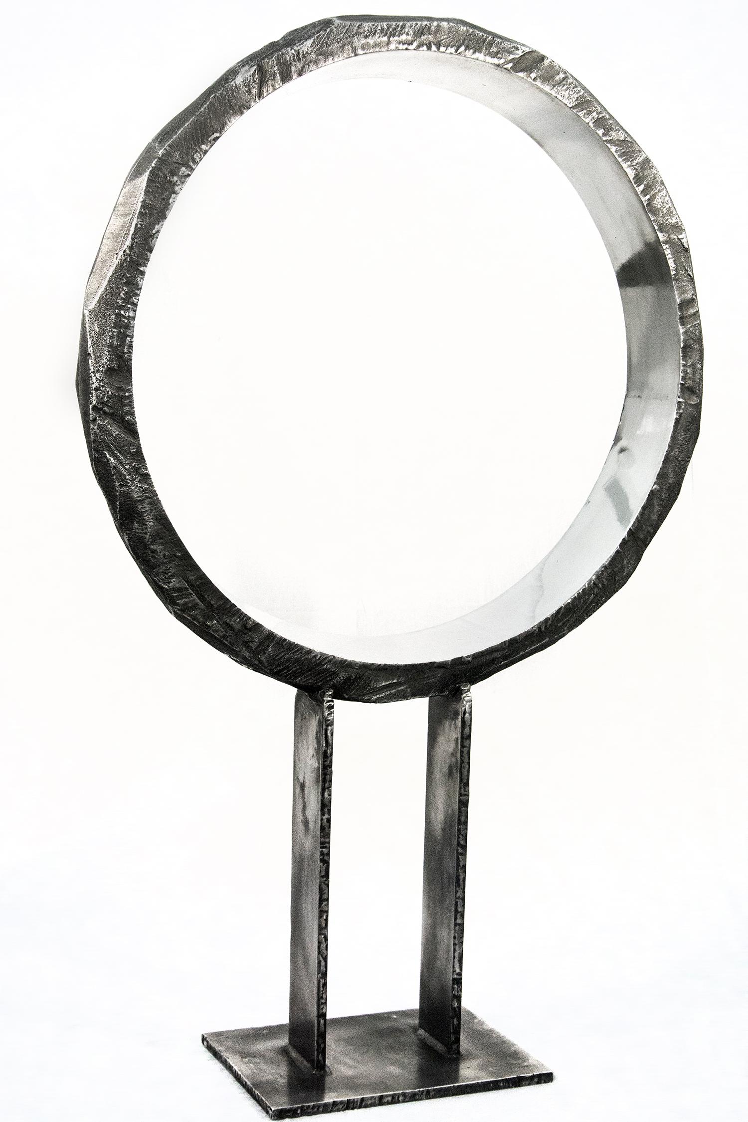 A large cast aluminum ring, polished and reflective on the inside and textured on its exterior elegantly frames the indoor space. Created by Philippe Pallafray and titled 