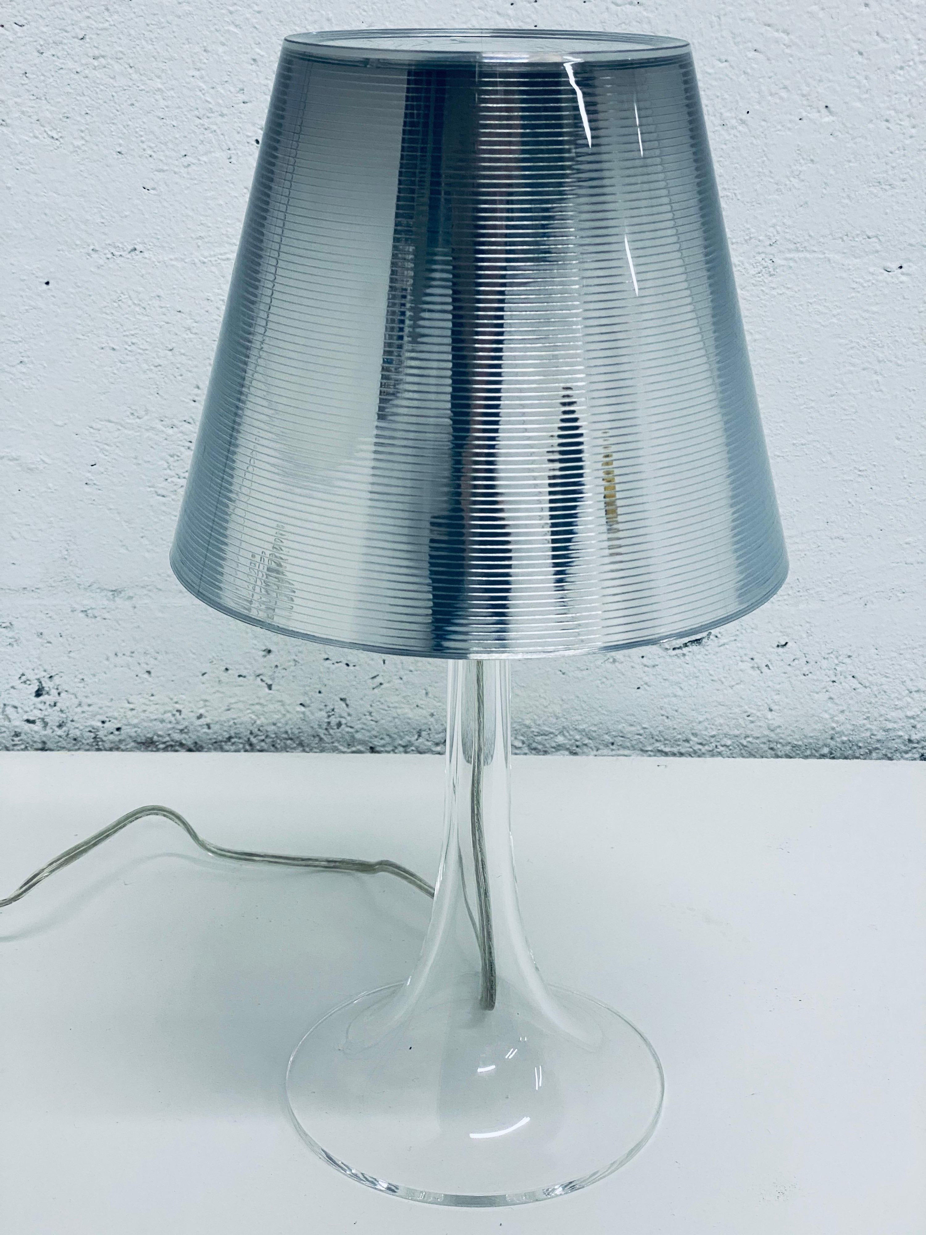 Miss K aluminized silver table or desk lamp designed by Philippe Starck for Flos.

Created by innovative design master Philippe Starck, the Miss K table lamp brings a delightful duality to its work. When unlit, its transparent PC (polycarbonate)