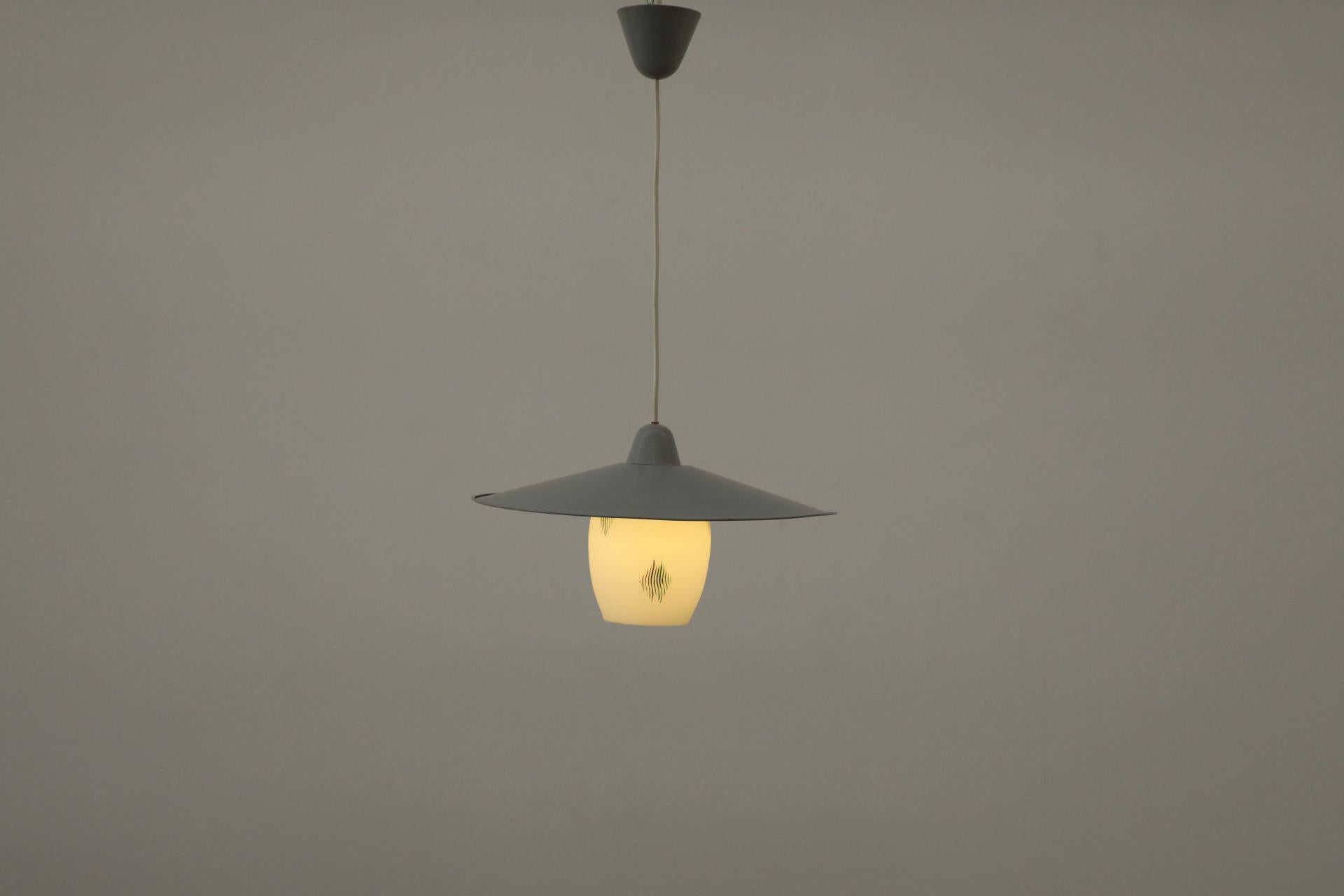 Splendido pendente a soffitto attribuito a Philips con paralume decorativo in vetro latte e cappello smaltato grigio. Il paralume in vetro lattiginoso presenta disegni decorativi dipinti degli anni '50-'60. Il paralume in metallo smaltato grigio