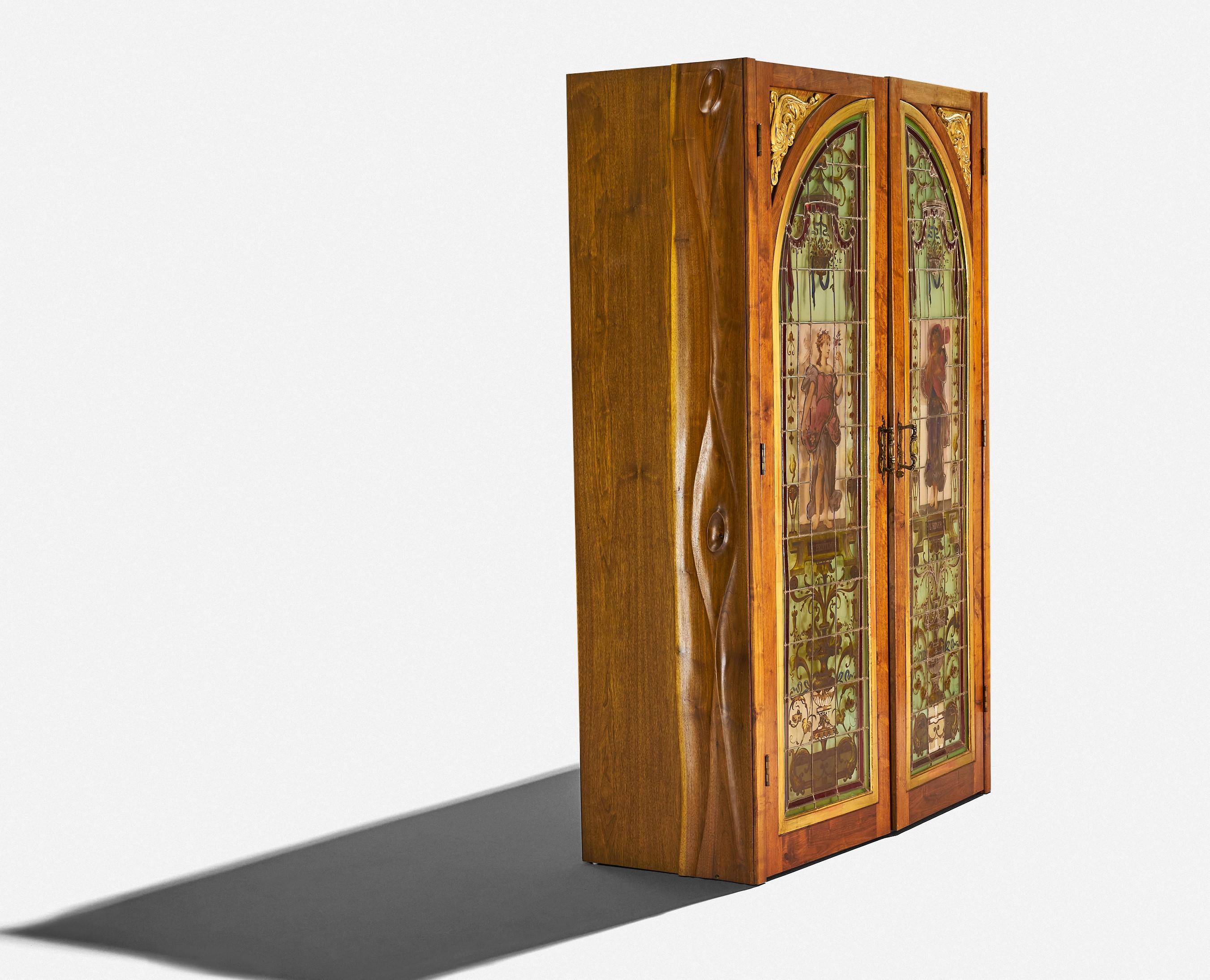 Phillip Lloyd Powell
illuminated bar cabinet
USA, 1970s
hand-carved walnut, glass, brass, found objects

One of one bench-made Phil Powell bar cabinet. Side panels are hand-carved walnut. Doors are stained glass with backlit lighting to