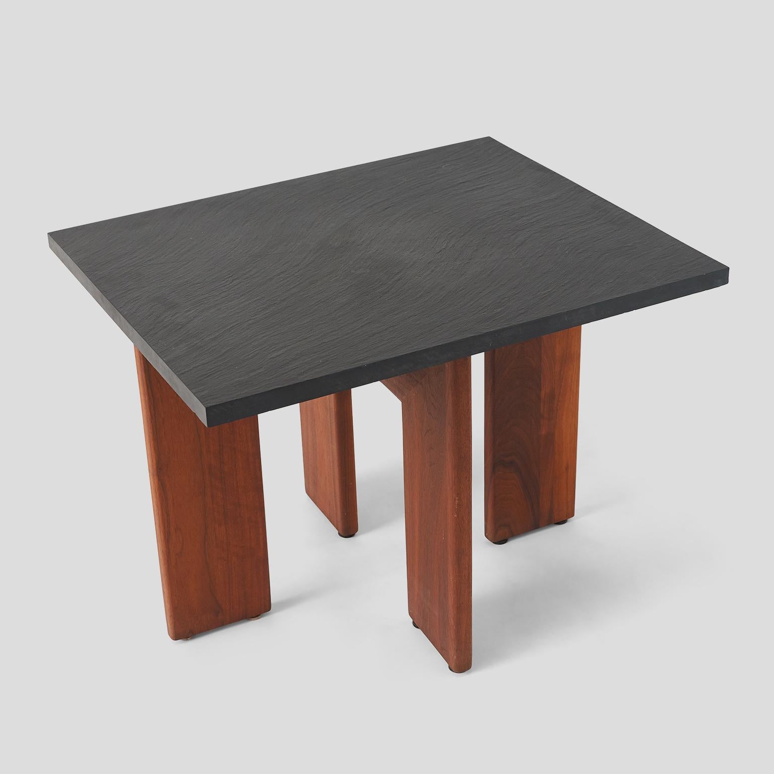 A gorgeous end table in American walnut with a grey stone slab top. Wide wooden legs forming a 