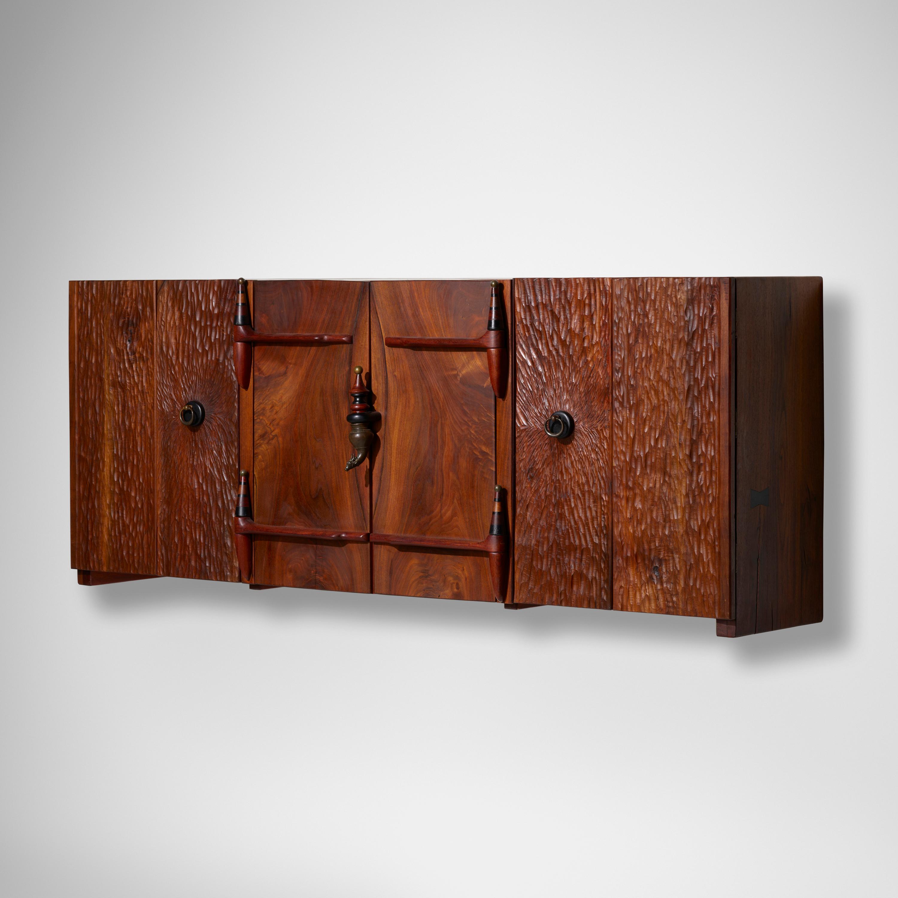 Phillip Lloyd Powell: Wall-Mounted Cabinet. Cabinet features 17th century finials and four doors (two bi-fold) concealing three adjustable shelves.

USA, c. 1995
Walnut, cocobolo, ebony, patinated metal, painted wood
30½ h × 78 w × 17 d in

