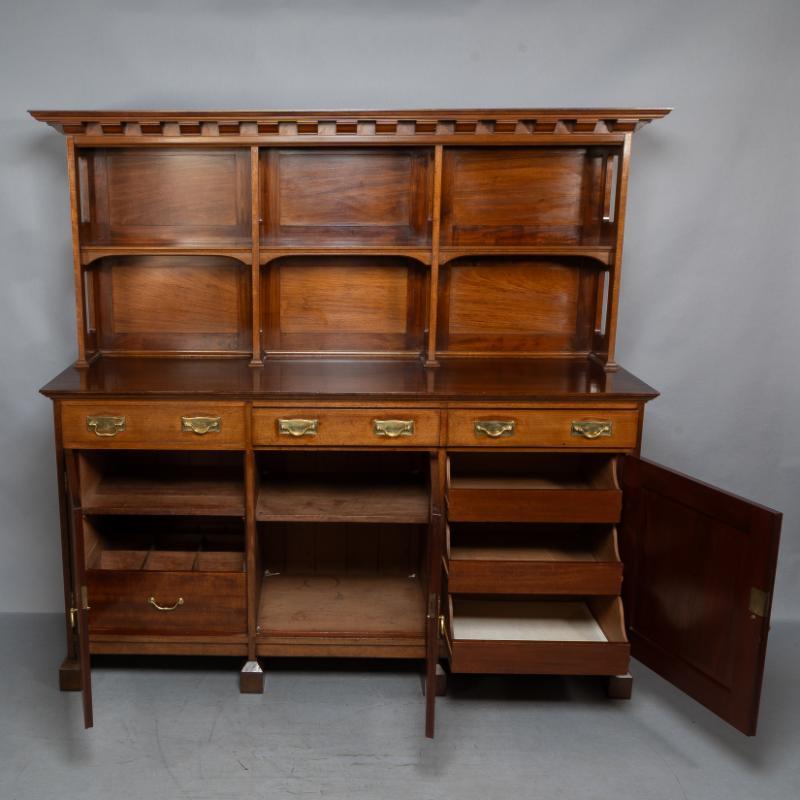 Morris & Co, zugeschrieben Philip Webb
Eine Anrichte im Stil des Aesthetic Movement aus Nussbaumholz im Arts and Crafts-Stil mit Zackenleiste am Gesims und offenen Regalen über der Arbeitsfläche. Mit zwei Schubladen, einer kleinen auf der linken