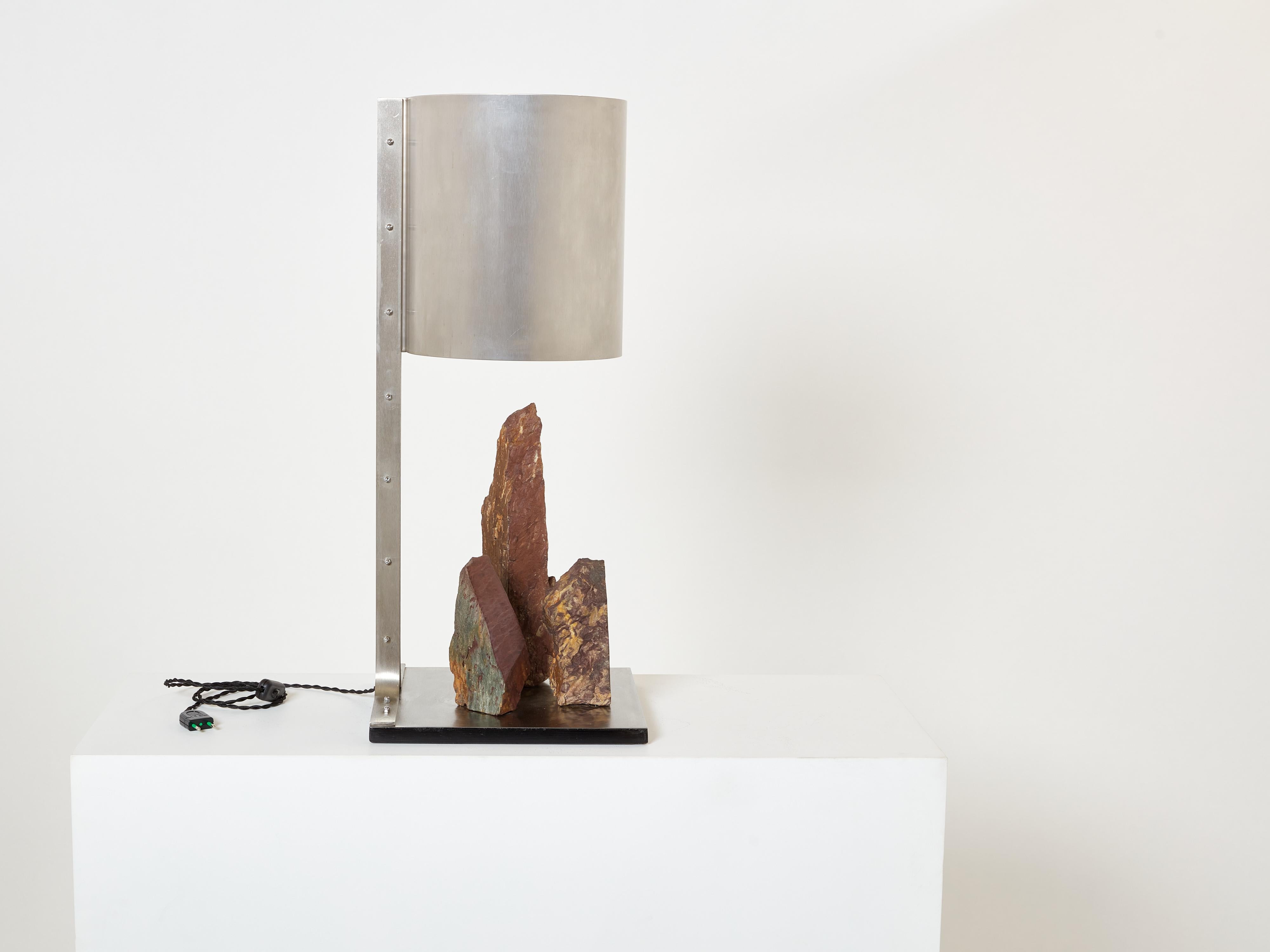 This brushed steel and red shale brutalist lamp is a unique piece signed by French sculptor Philippe Jean, produced in the early 1970s. Echoing the distinctive aesthetic of pioneer Maria Pergay, the cylindrical and minimalist form of this lighting