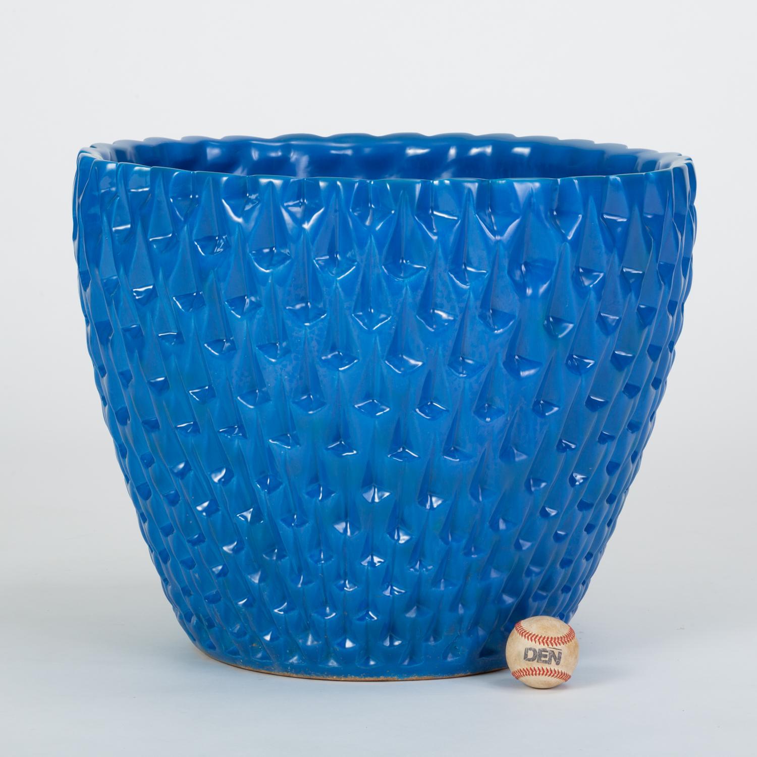 Designed by David Cressey in 1963 as part of the Pro/Artisan stoneware collection for Architectural Pottery, the slipcast Phoenix planter has a bowl shape with an allover geometric relief. This example is has a cerulean blue glaze with a glossy