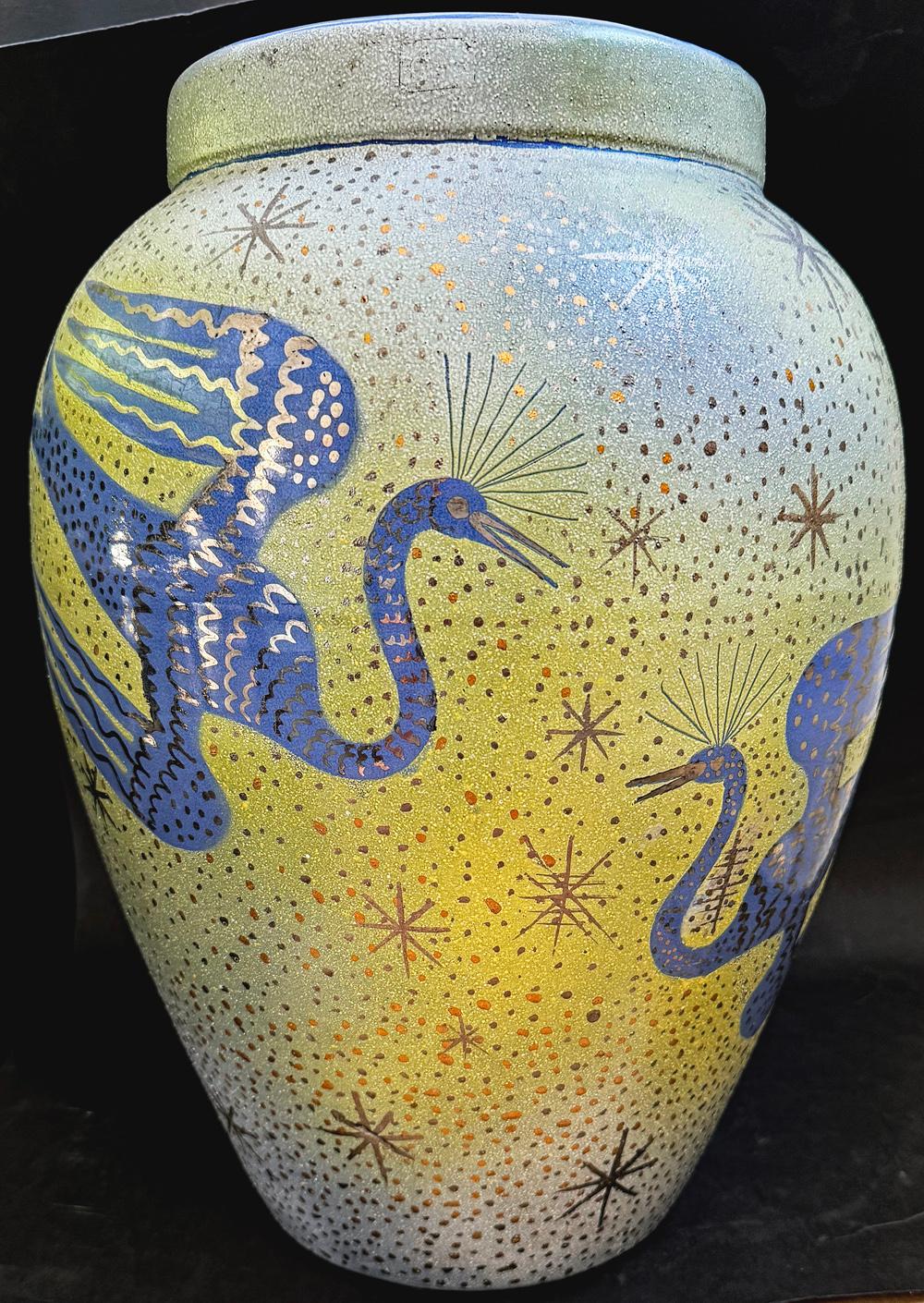 Grande e imponente, questa urna Art Déco unica di Waylande Gregory raffigura due uccelli fenice in volo, con ali spiegate e piume brillanti nei toni del pervinca intenso e dell'argento.  Il fondo è smaltato con una sfumatura di verde e blu,