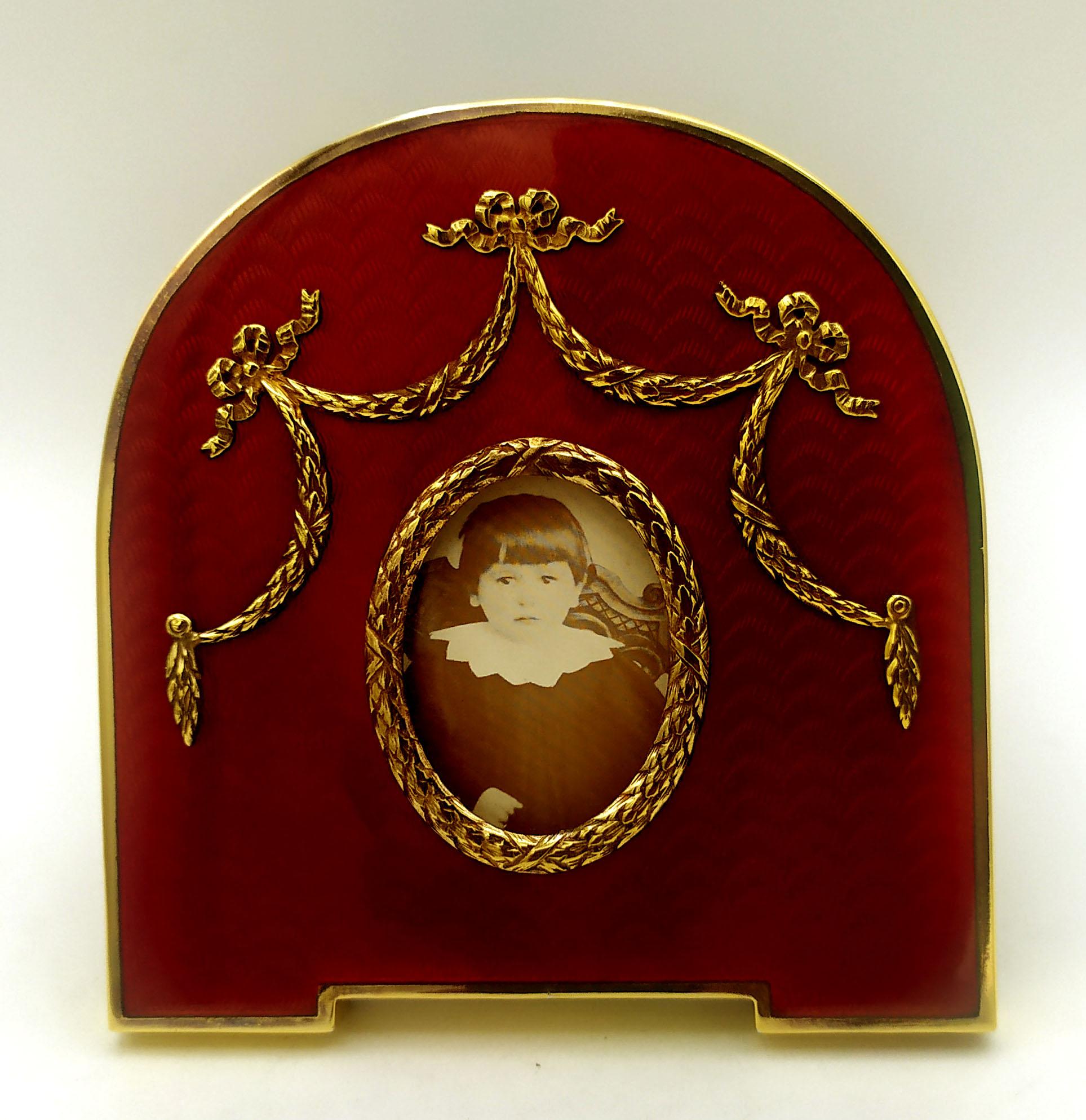 Ovaler Fotorahmen aus vergoldetem 925/1000er Sterlingsilber mit durchscheinendem, gebranntem Email auf Guillochè und Ornamenten im Louis XVI-Stil des französischen Empire. Außenmaße cm. 13.5 x 11. Innen oval cm. 3.2 x 4.2. Gewicht gr. 158. Entworfen