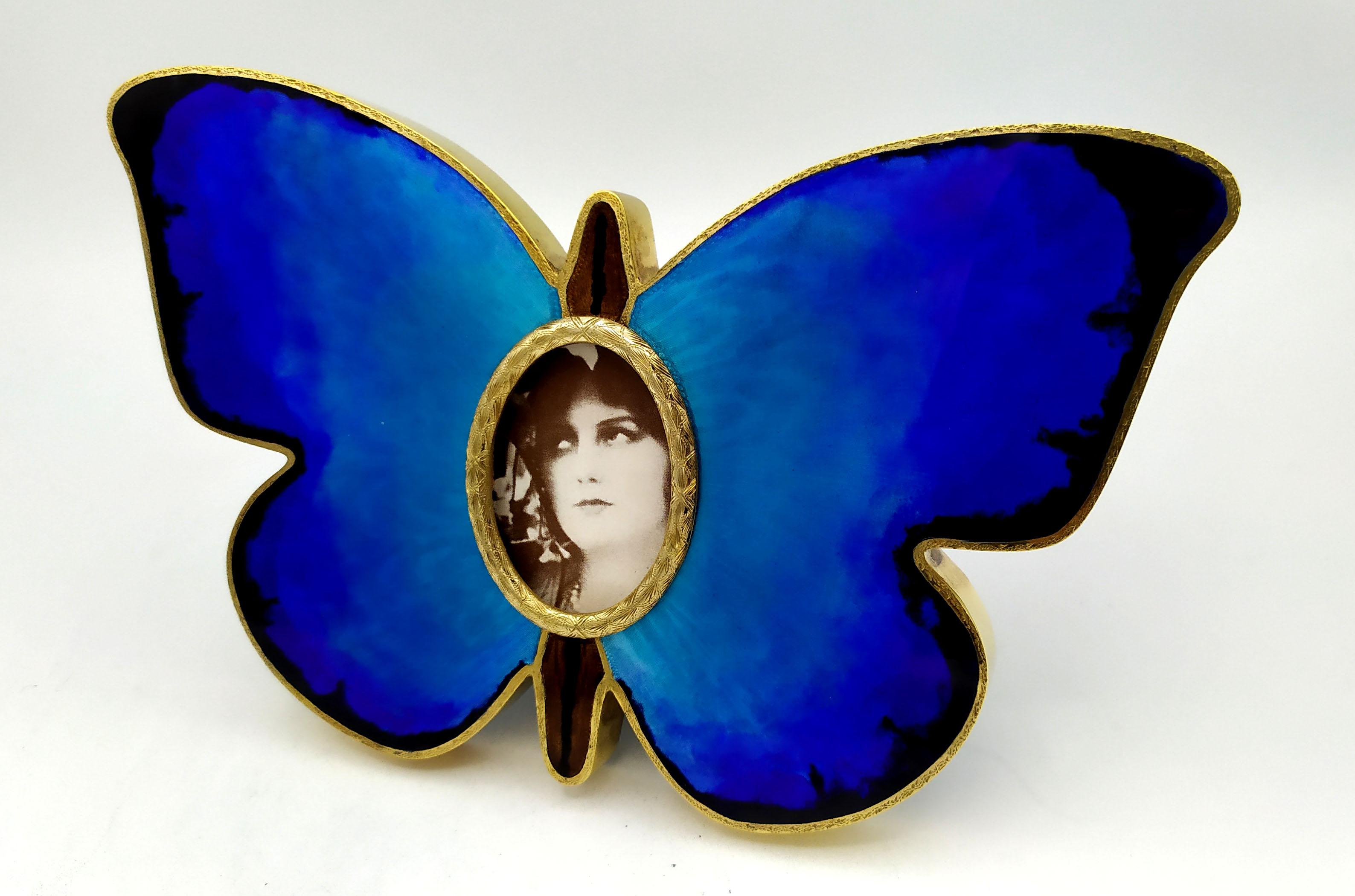 Butterfly-shaped photo frame in 925/1000 sterling silver gold plated with translucent polychrome fired enamels on hand engraving that imitates the veins of the wings. External dimensions cm. 12 x 19 oval for photos cm. 3.2 x 4.5. Weight gr. 220.
