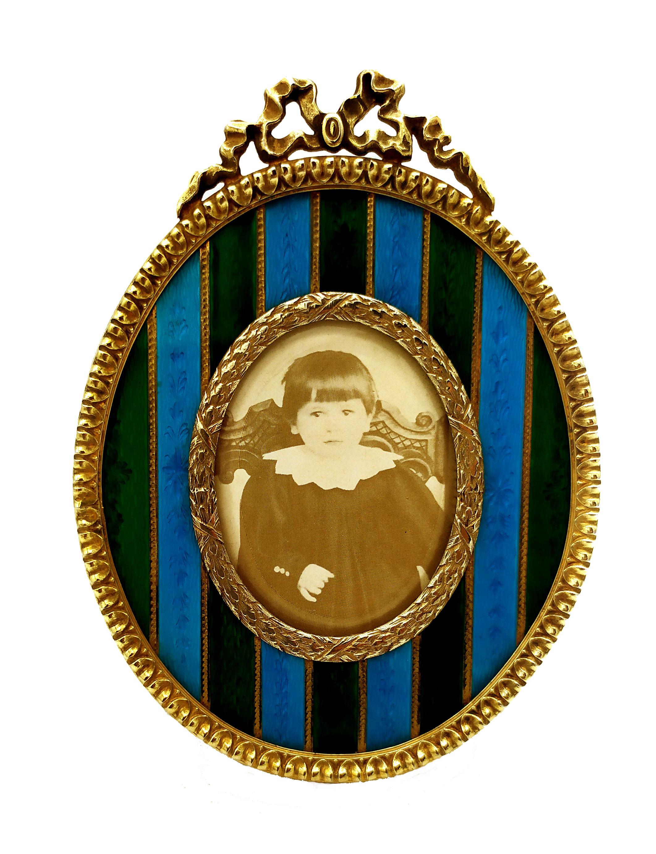 Marco oval  de plata de ley 925/1000 bañada en oro con bandas translúcidas bicolores esmaltadas al fuego sobre guillochè y grabadas a mano y con adornos estilo Imperio Francés Napoleón III. Medida exterior cm. 8,8 x 12 interior cm. 4 x 5.3. Peso gr.