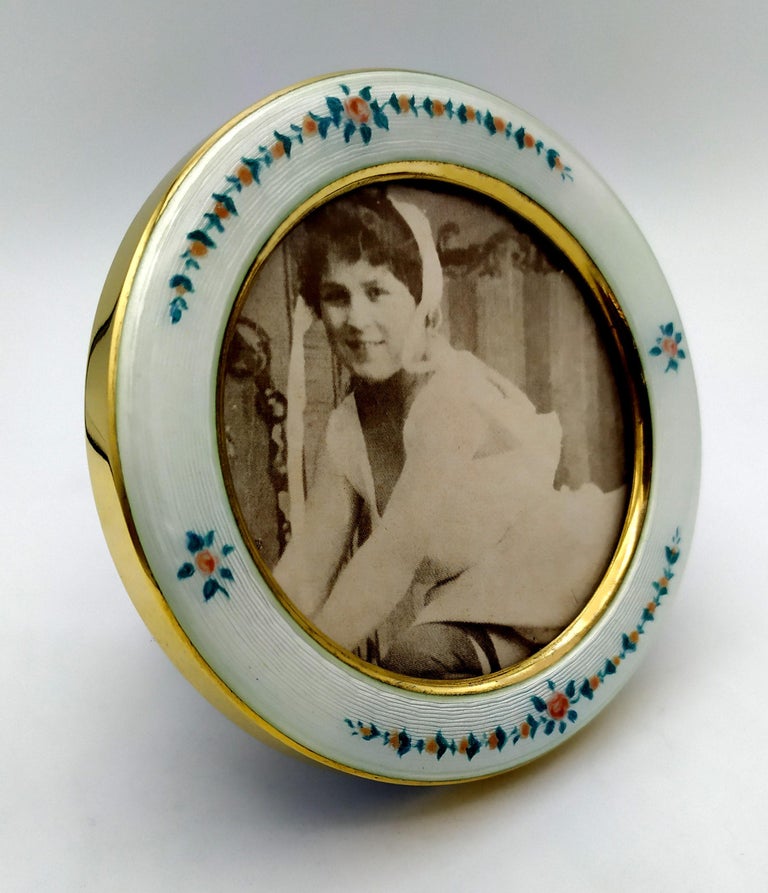 Round photo frame in 925/1000 sterling silver gold plated with translucent fired enamel on guillochè and hand-painted miniature of late 19th-century Viennese Art Nouveau-style flower garlands. Outer diameter cm. 10 inside cm. 6.8. weight gr. 77.