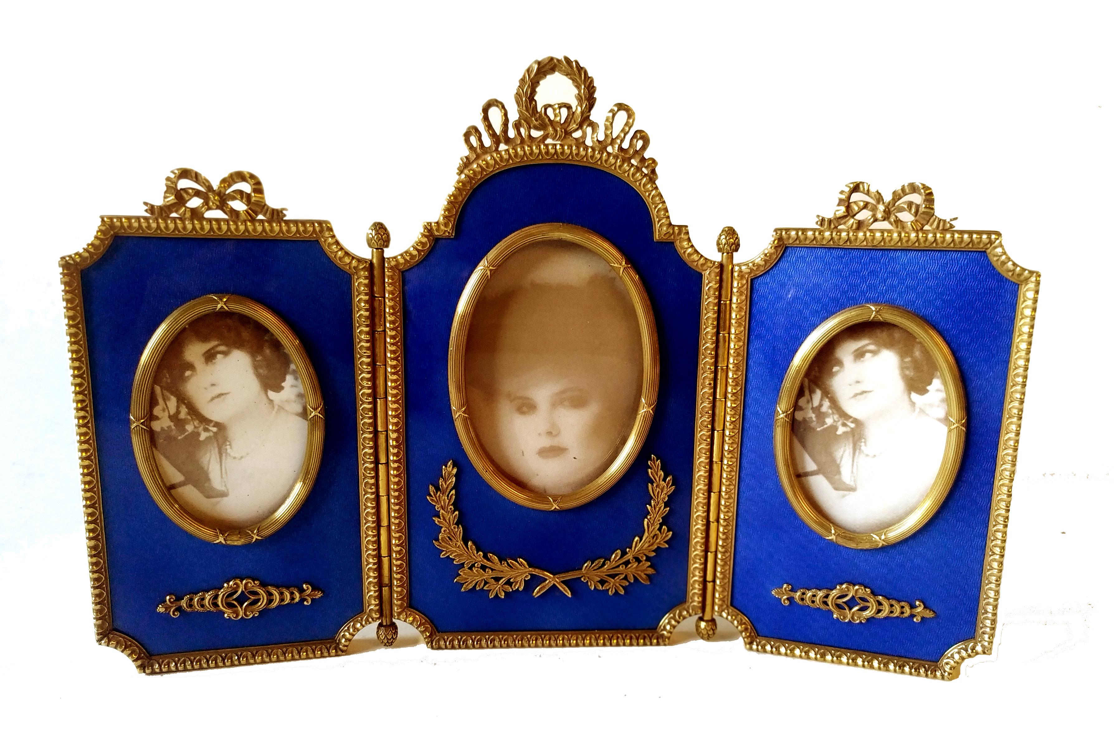 Triptych hinged shaped frame for 3 photographs in 925/1000 sterling silver gold plated  with translucent fired enamel on guillochè with borders and ornaments in French Louis XVI Empire style. Open measurements 27.7 x 18.2 cm. Weight gr. 877.
