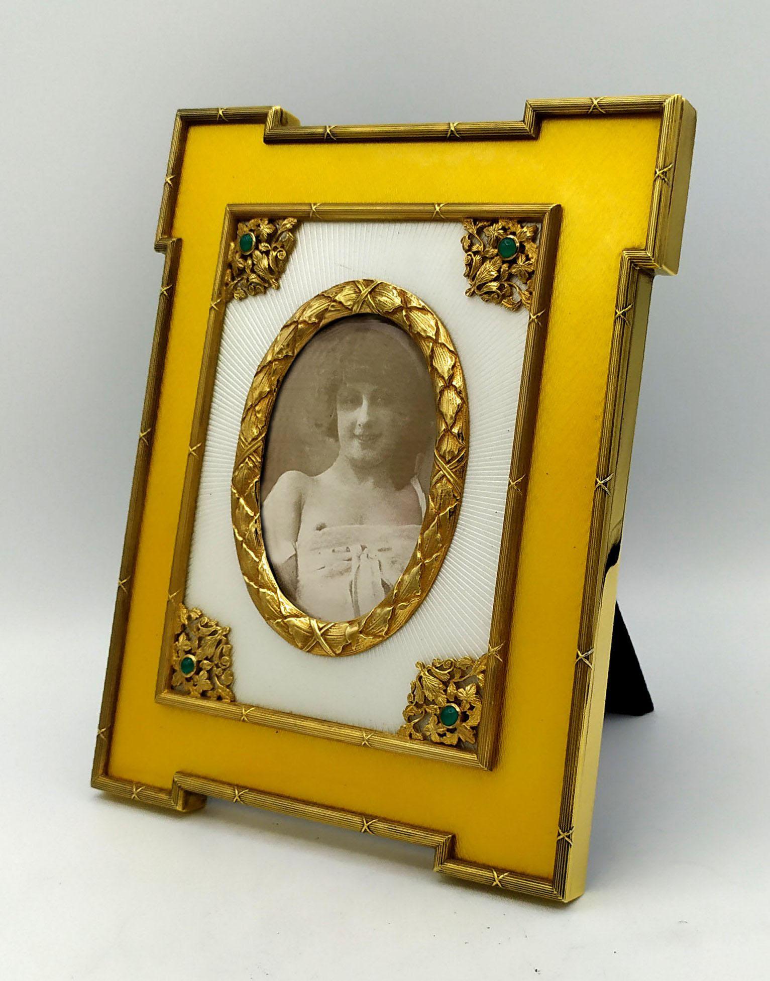 Large shaped photo frame in 925/1000 sterling silver gold plated with translucent two-tone fired enamel on guillochè and with various ornaments in Louis XVI French Empire style and 4 round cabochon emeralds mm. 5. External dimensions cm. 18.5 x 21.5