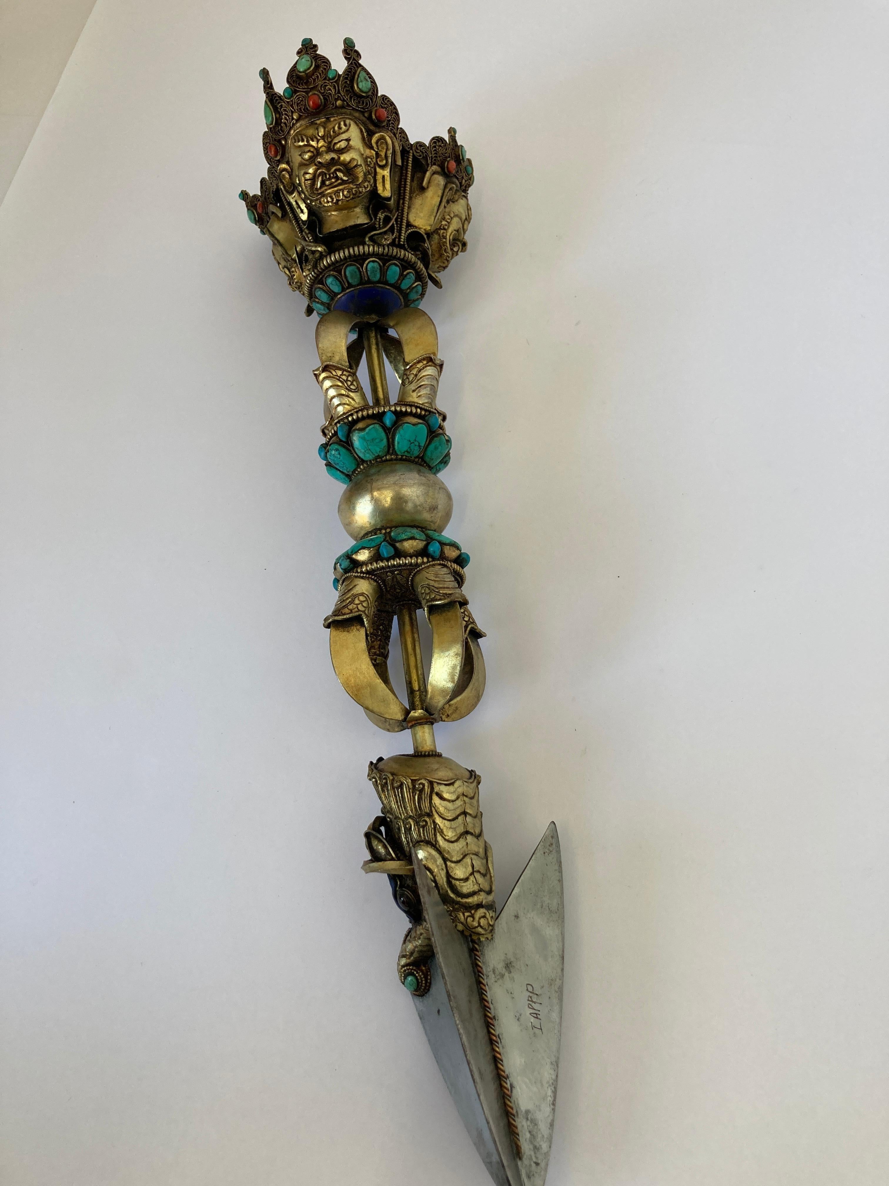 Large Phurba ornate with semi precious stones, like turquoise and red stones incrusted in brass metal.
The Phurba or Kila: the most potent of wrathful ritual implements in Vajrayana Buddhism, symbolizes the Karma activity of the Buddhas.
Contrary