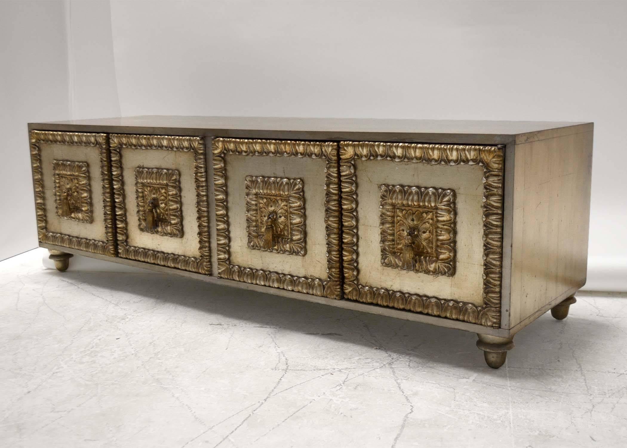 A low cabinet by Phyllis Morris with and antiqued silver leaf finish. Four doors with over the top trim and tassel pulls. The pinnacle of Hollywood Regency Style!