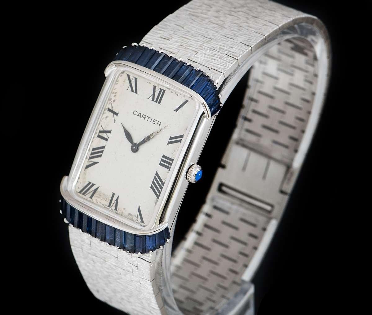 A 23 mm 18k White Gold Retailed by Cartier Vintage Ladies Wristwatch, silver guilloche dial with roman numerals signed by Cartier, a fixed 18k white gold bezel, an 18k white gold case set with approximately 15 sapphires on each side (total of