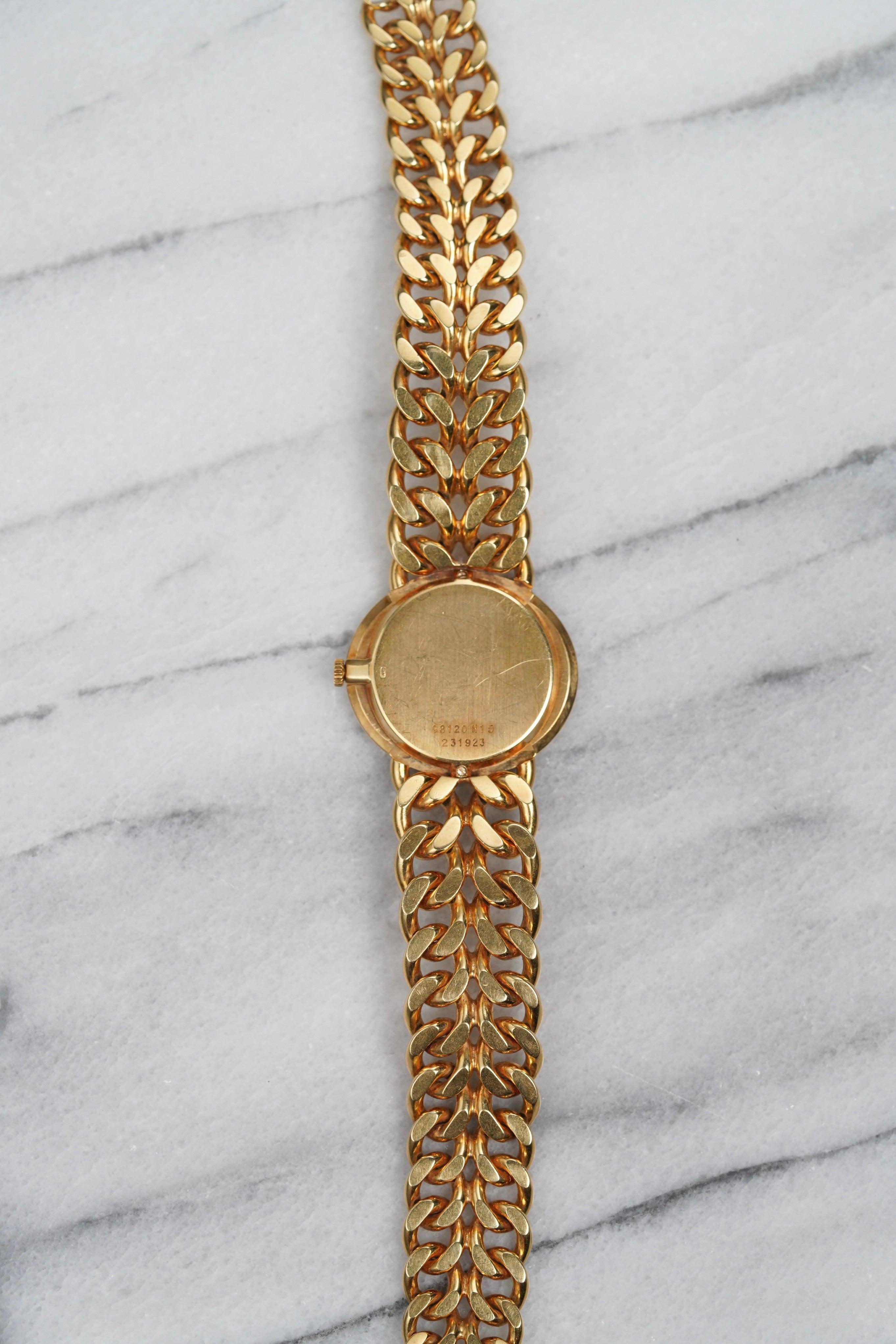Here's a vintage Piaget manual wind reference 98120 in 18K yellow gold with a roman numeral tiger eye dial from the 1980s. Measurements include a 26mm case and a bracelet that fits up to a 6.75 inch wrist. Time only. Dauphine hands. Curb style chain