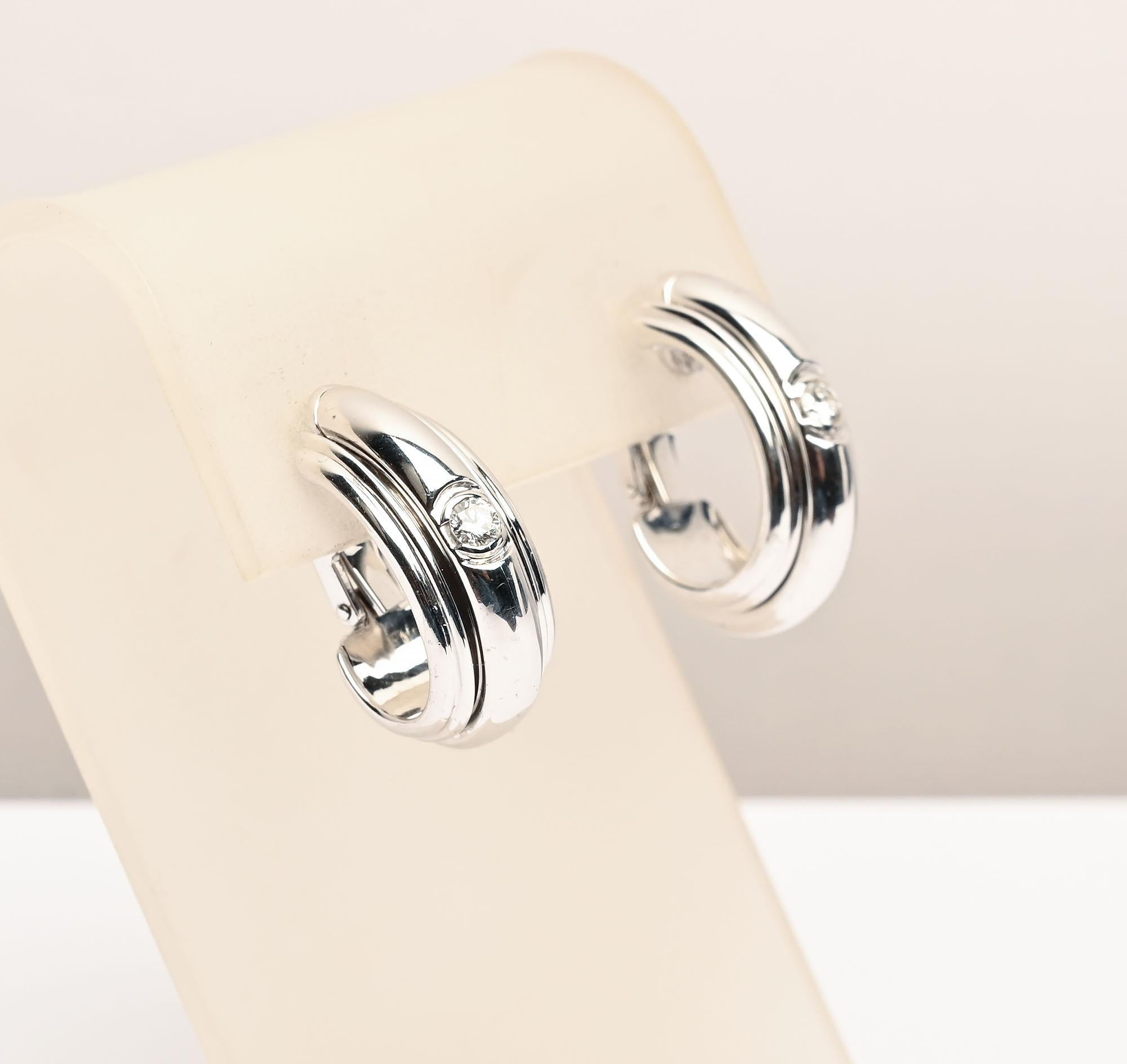 Piaget white gold 18 karat half hoop earrings with a .25 carat diamond in the middle of each. The diamonds are set in a raised band that intentionally can move. A double ribbed gold outlines the middle raised band. In all,  the earrings have a very