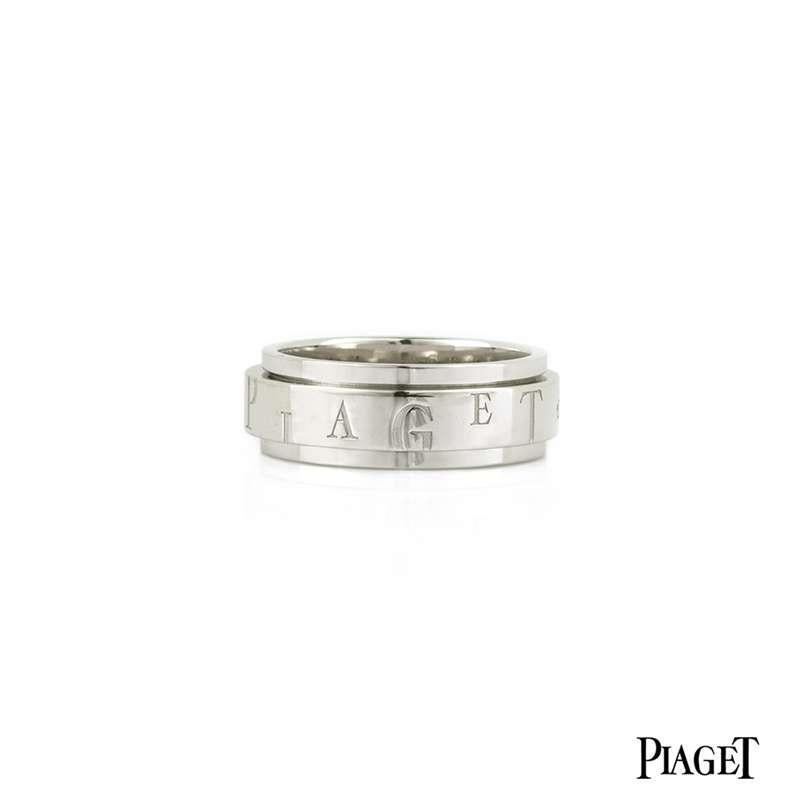 An 18k white gold Possession ring by Piaget. The 7mm step design ring features a middle band, which moves freely in perpetual movement. The central band is engraved with 'Piaget' twice, each letter alternating in height. The band is set with 2 round