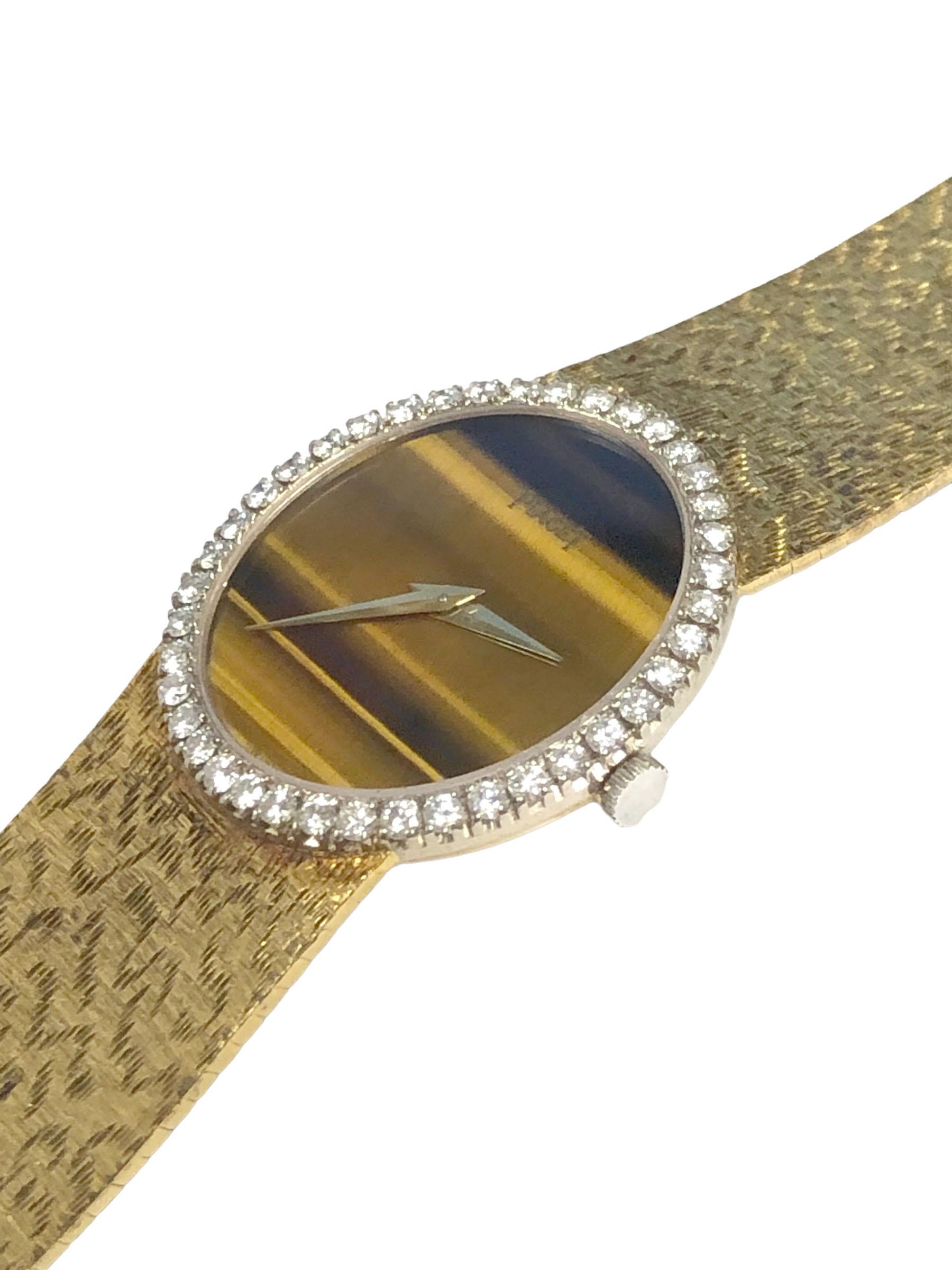 Circa 1970s Piaget Ladies Wrist Watch, 27 X 24 M.M. 18k Yellow Gold 2 piece case, White Gold Bezel with Round Brilliant cut Diamonds totaling 1 Carat. 17 Jewel mechanical, manual wind movement, Tiger Eye Dial. Textured integrated bracelet, watch
