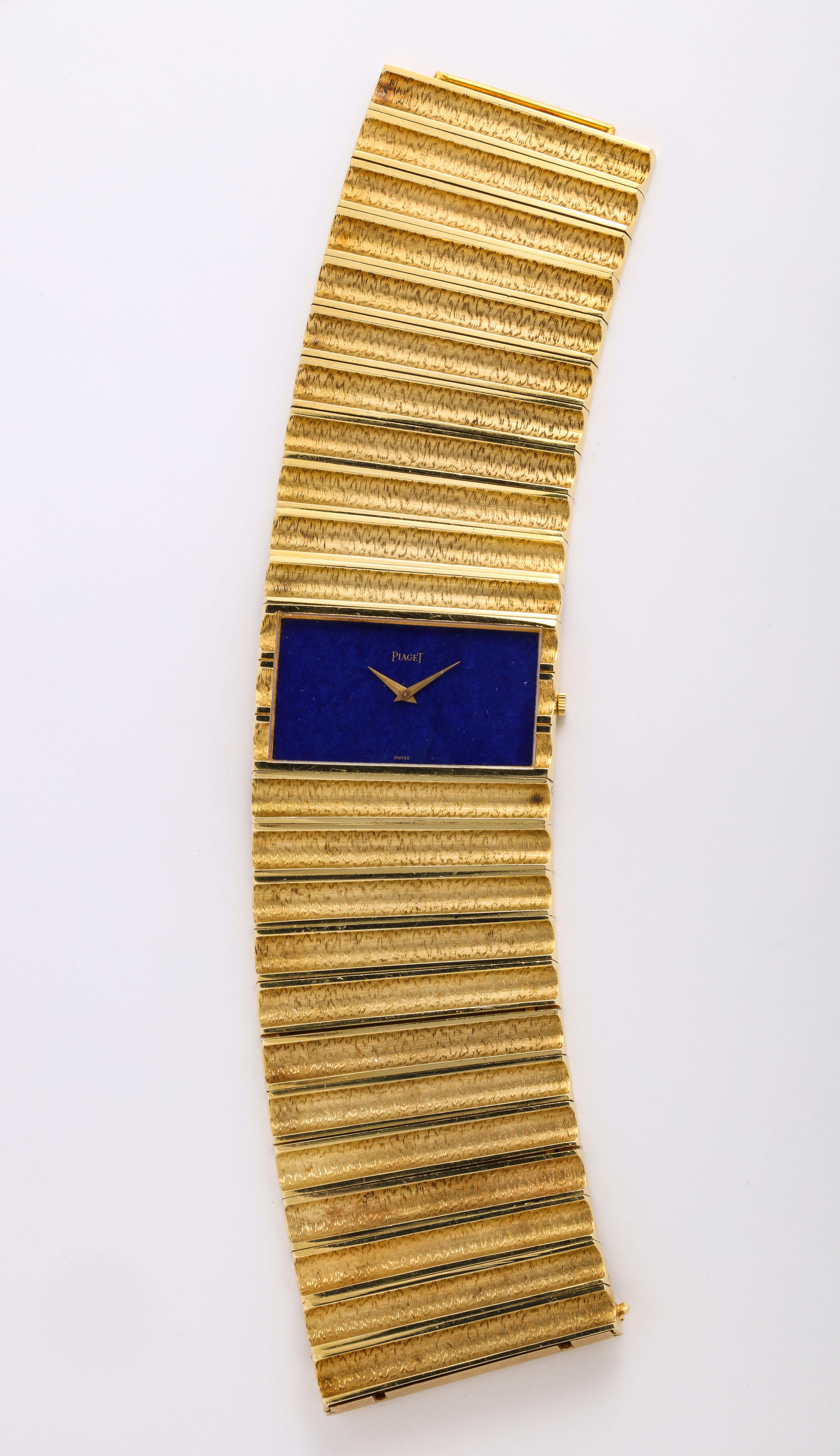 A bold watch by Piaget, created in 18k yellow gold with a rectangular lapis dial, measuring 7 ½ long x 1 ¾ wide. 125.6 dwt. The clasp is marked Piaget 750. 

Material: 
18k Yellow Gold

Stone:
Lapis

Markings:
Marked 9000 D78 / 173499 ©