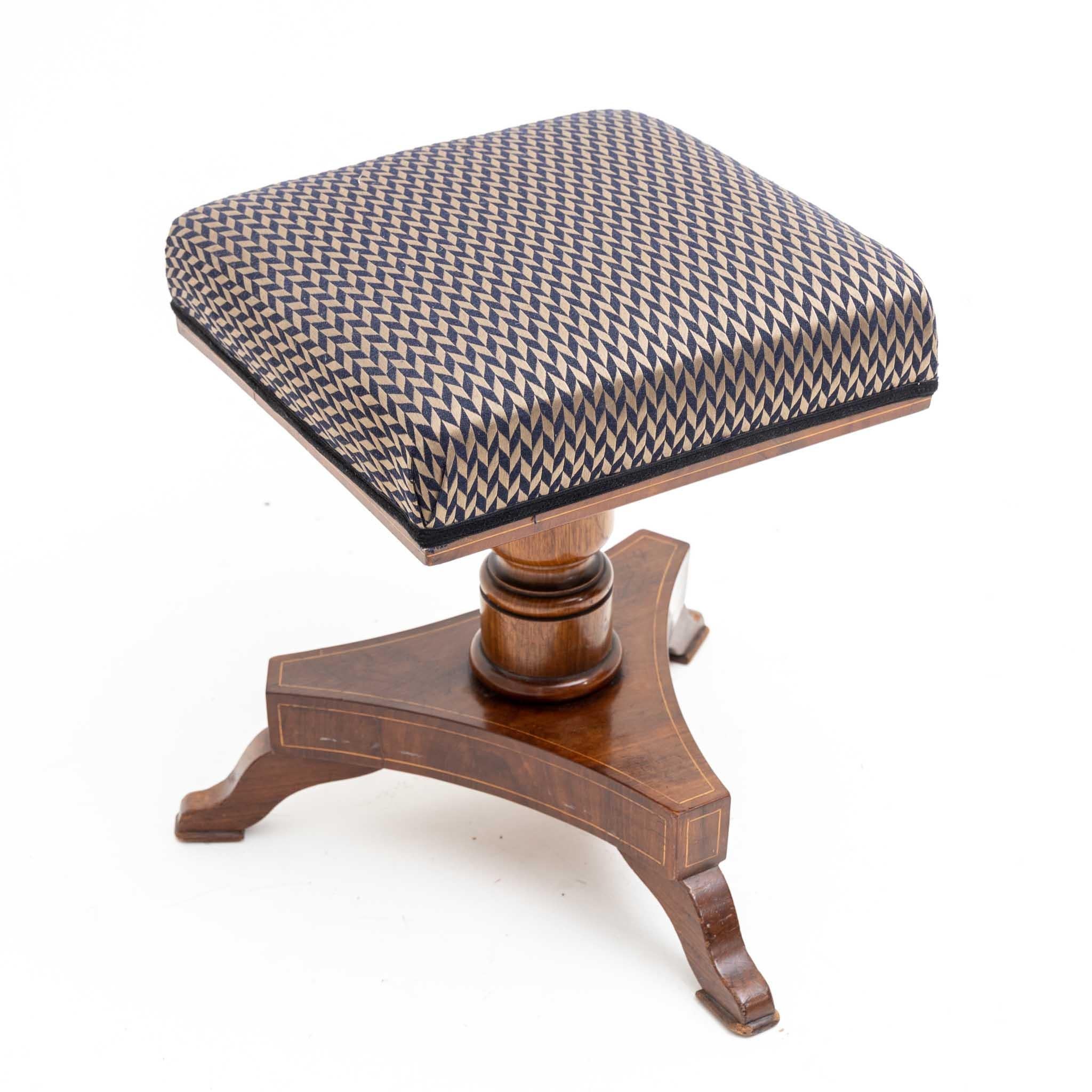 Piano stool on a trefoil stand with low S feet and square seat. The stool is veneered in mahogany with thread inlays and has been reupholstered. Uninterpreted royal monogram on the underside.