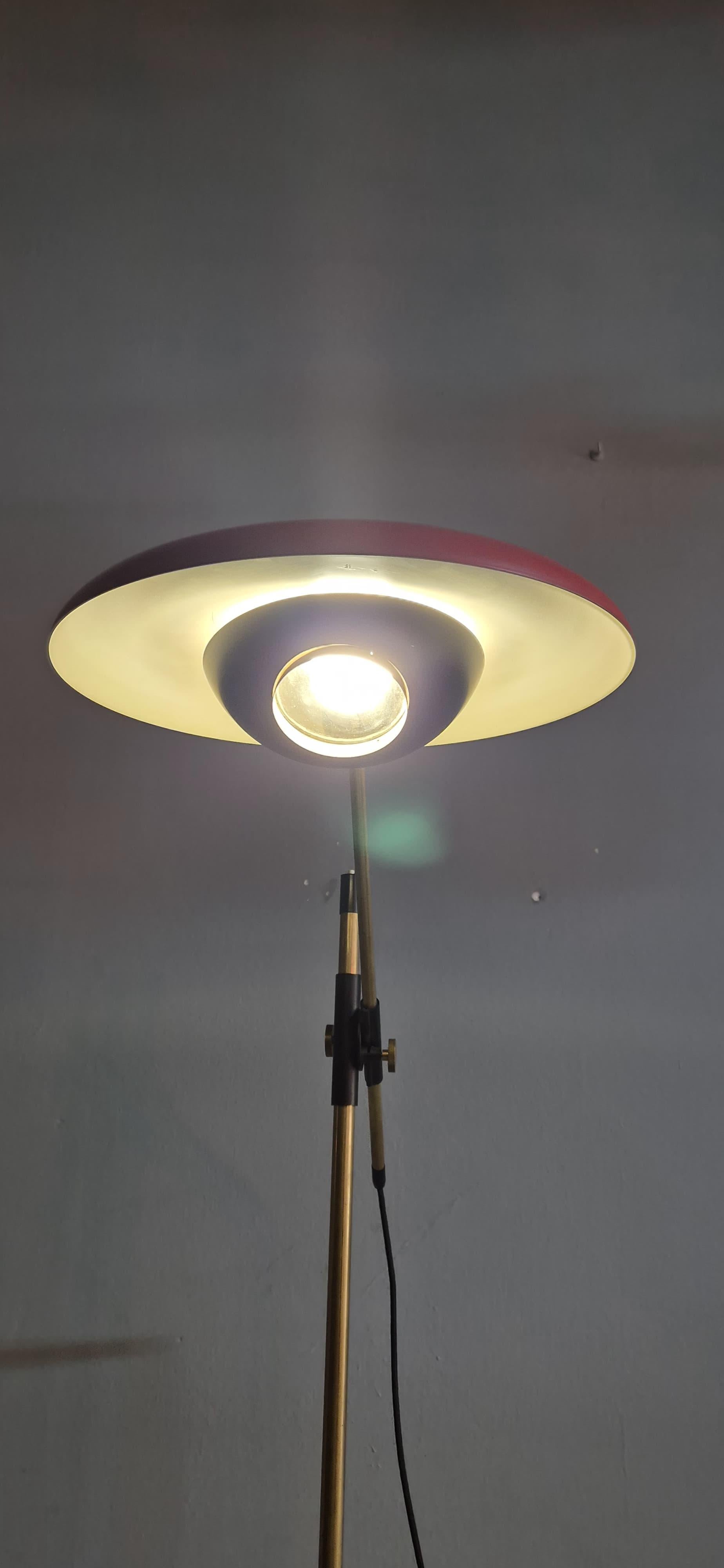 Preciosa lámpara de pie de mediados de siglo diseñada por Oscar Torlasco para Lumi Milano. La lámpara tiene una estructura de brazo ajustable de latón con una pantalla de metal pintado de rojo y una lente de cristal que encierra la bombilla; el