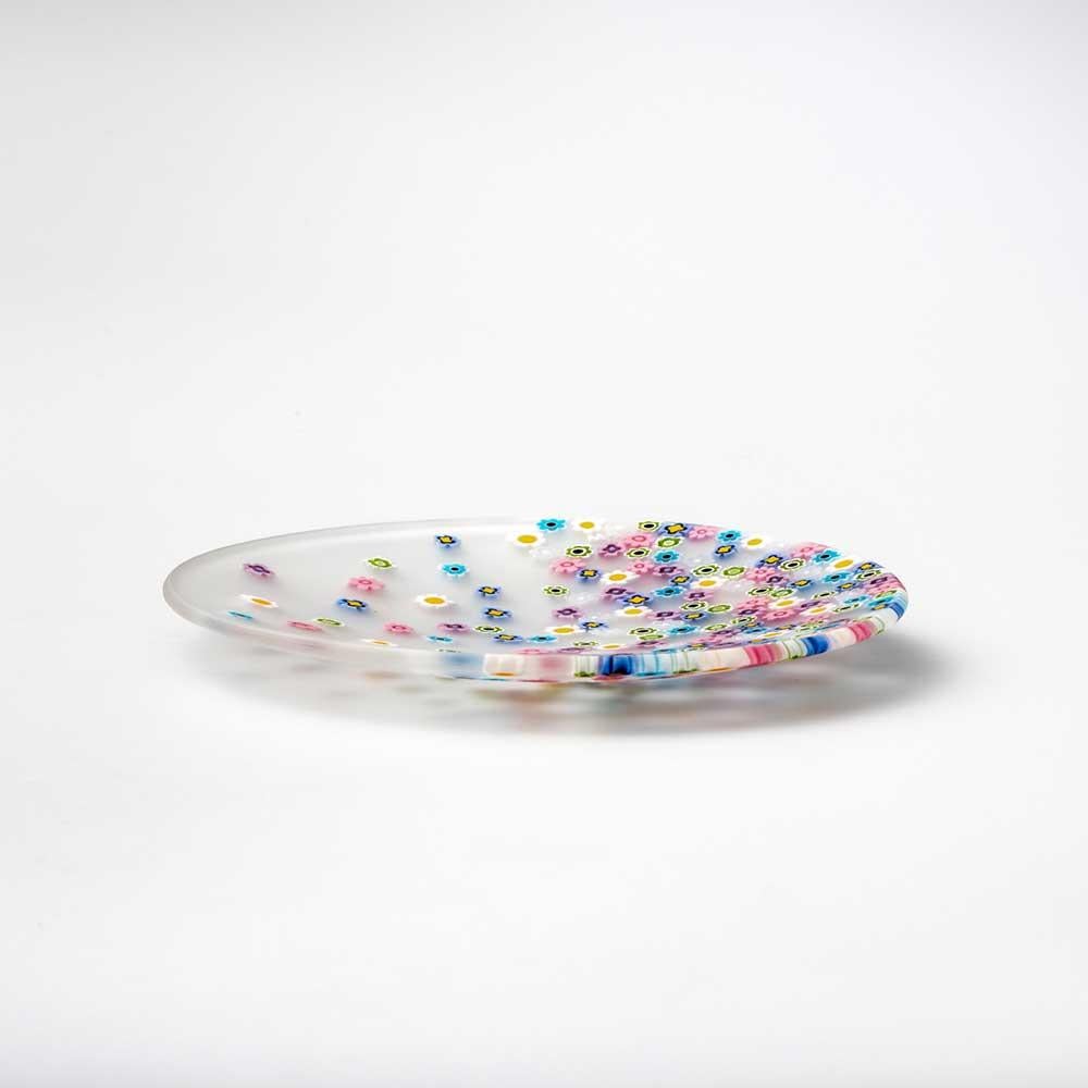 Il vento di primavera sparpaglia le murrine che decorano questo piatto, come una brezza leggera. Creato dal designer Paolo Cappello, è realizzato con la tecnica del “vetro murrino millefiori” che fonde insieme segmenti di bacchetta di vetro, ognuno