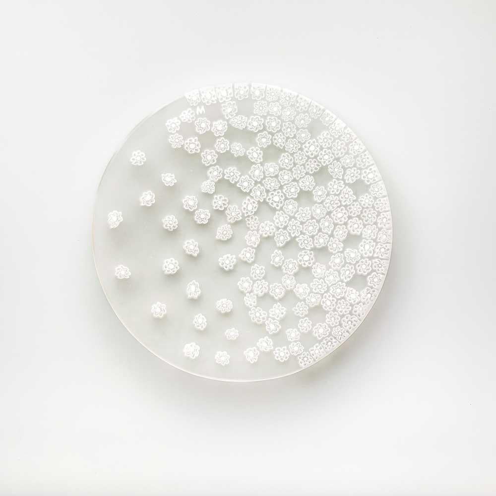 Con il soffio della primavera, le murrine sul piatto si disperdono come in un gioco a rincorrersi. Questo capolavoro del designer Paolo Cappello è realizzato con la tecnica del “vetro murrino millefiori”, che intreccia segmenti di bacchetta di vetro