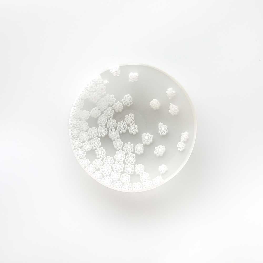 Con il soffio della primavera, le murrine sul piatto si disperdono come in un gioco a rincorrersi. Questo capolavoro del designer Paolo Cappello è realizzato con la tecnica del “vetro murrino millefiori”, che intreccia segmenti di bacchetta di vetro