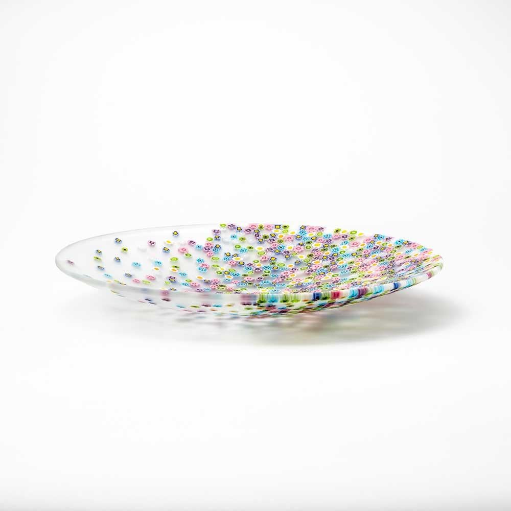 La leggera brezza primaverile disperde le murrine sul piatto in una delicata coreografia. Questo piatto in vetro di Murano firmato dal designer Paolo Cappello, è realizzato con la tecnica del “vetro murrino millefiori”, combinando segmenti di
